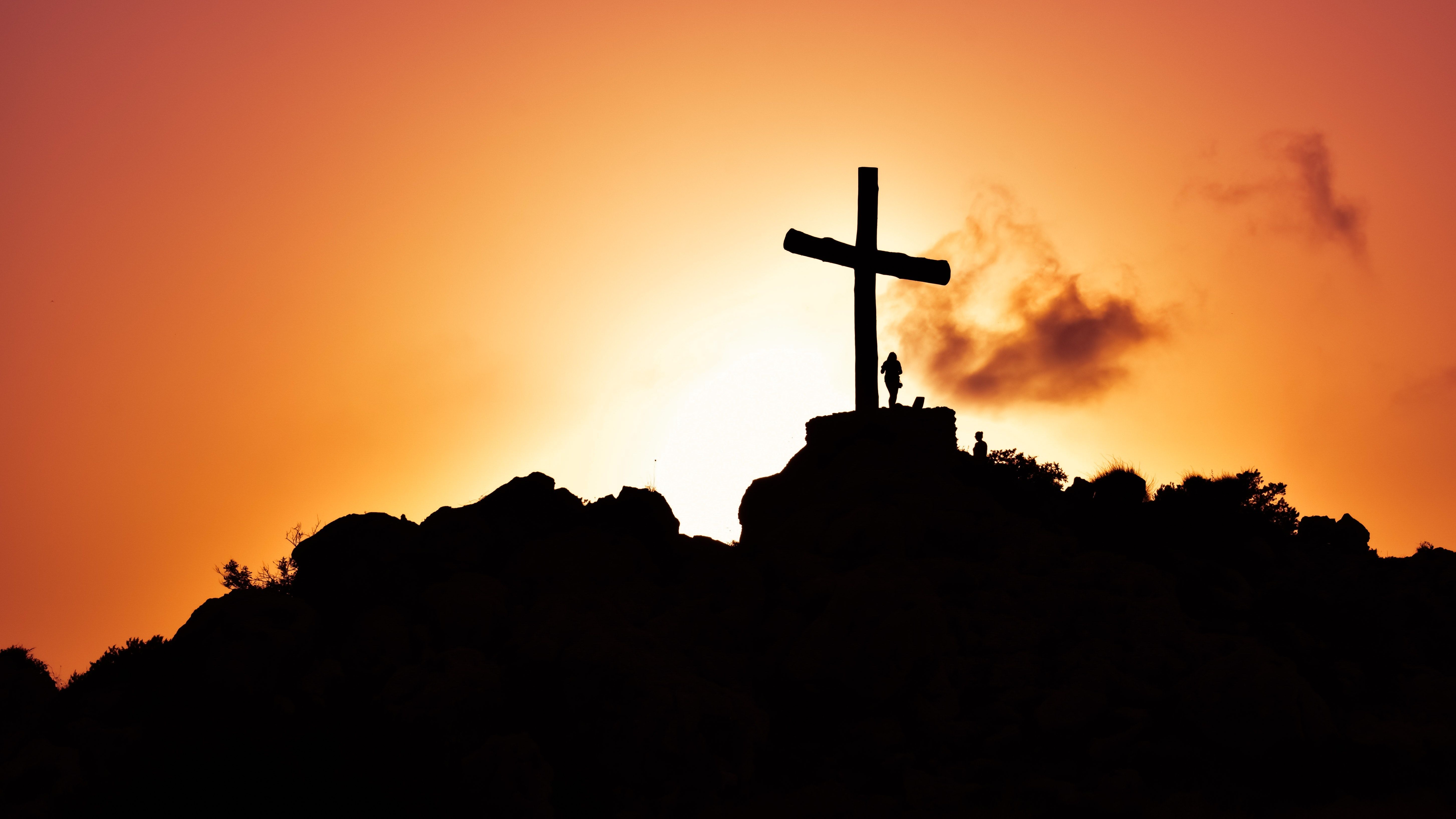 A silhouette of a cross on a hill with a couple standing on it. - Cross