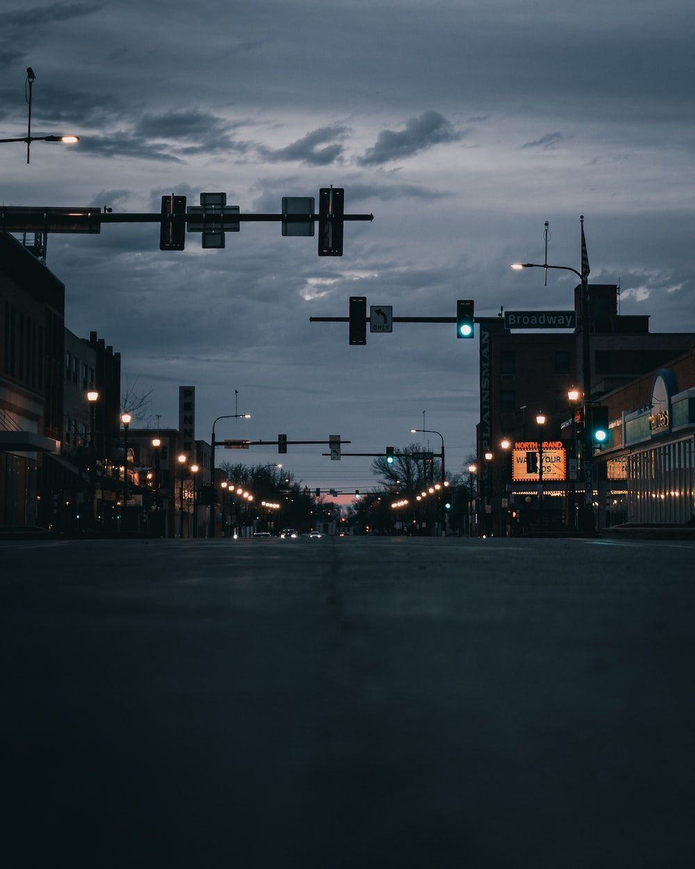 A dark street with traffic lights and street lights on a cloudy evening - Broadway