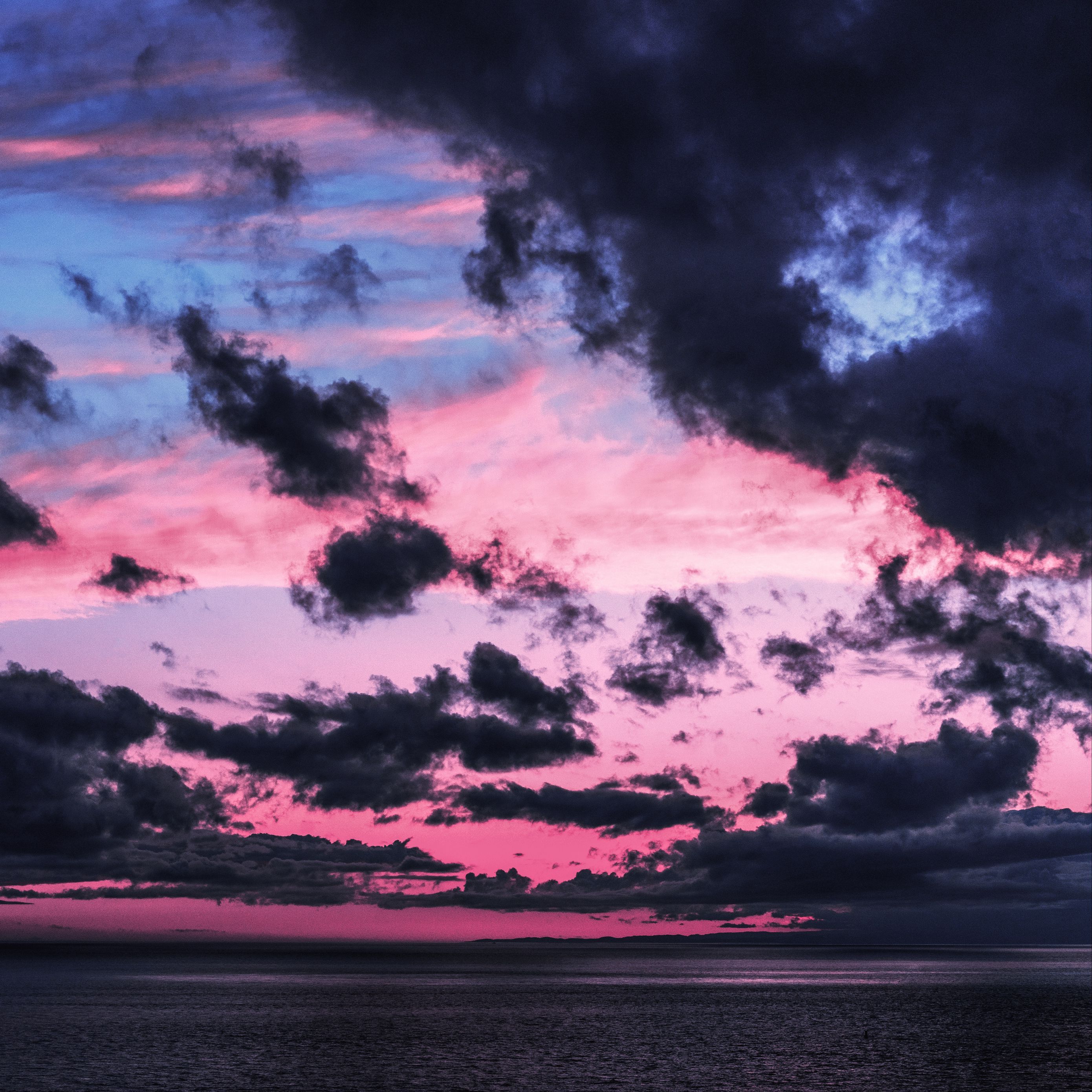 A dramatic pink and blue sunset over the sea, with dark clouds gathering. - Twilight