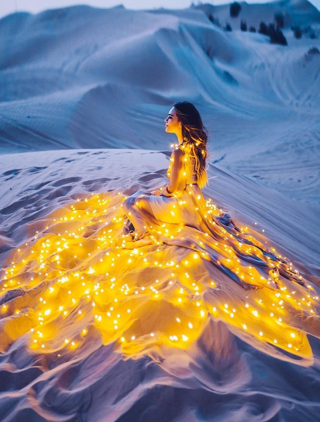 A woman sitting in the sand with lights on her - Yellow iphone, fire