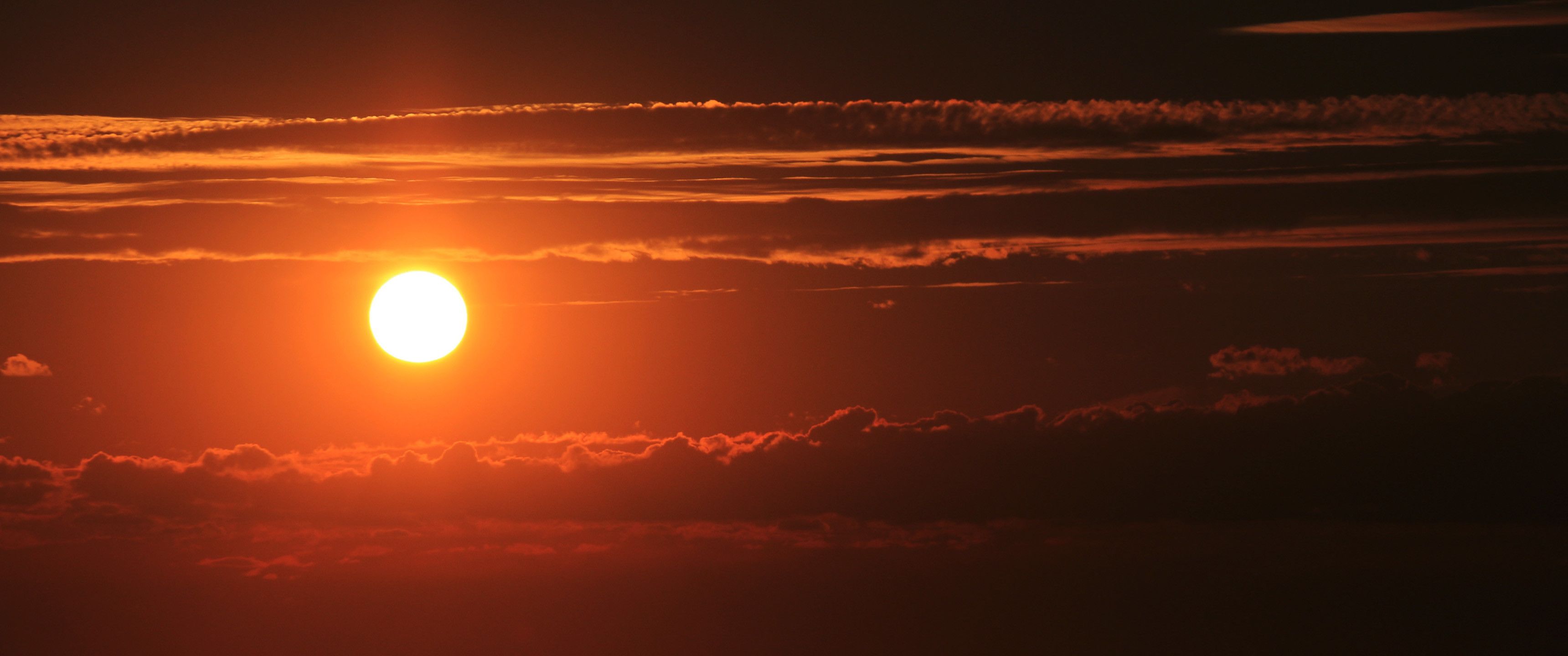 A sun setting behind a layer of clouds. - 3440x1440