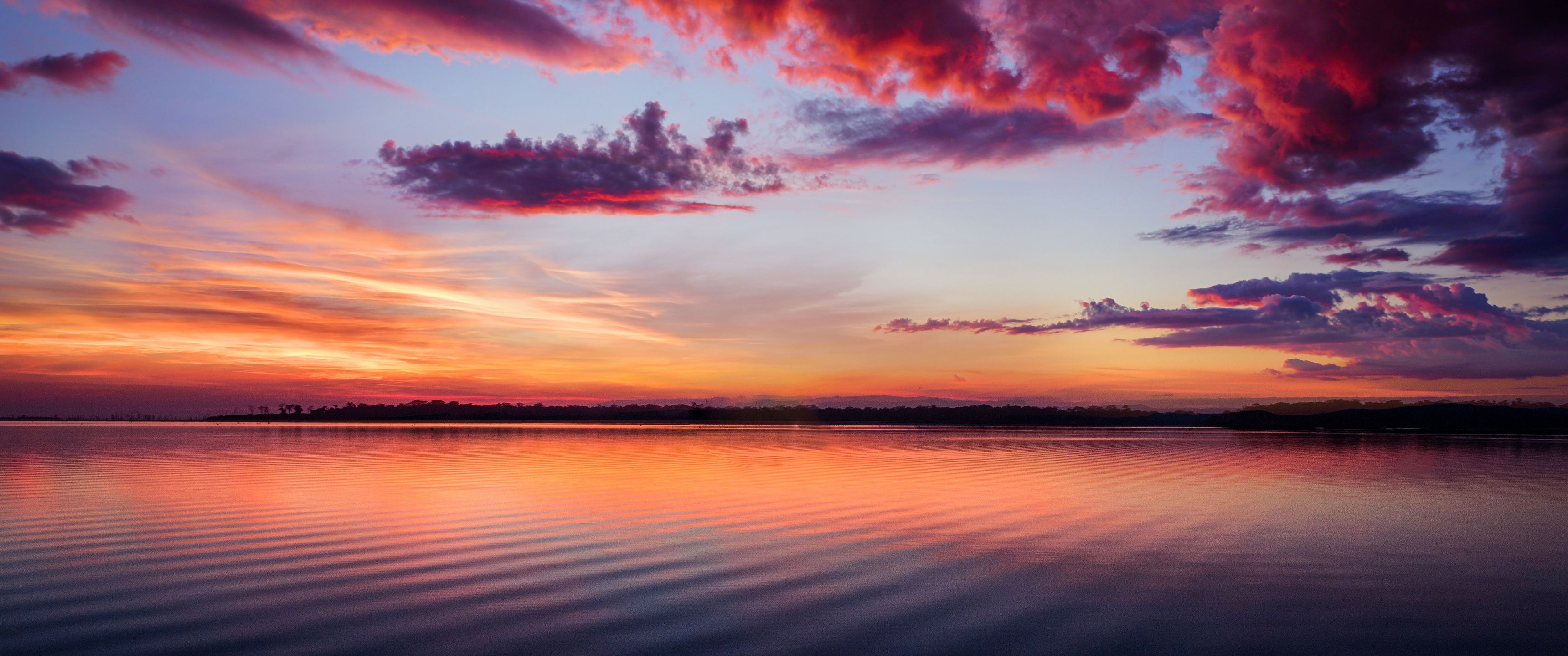 A sunset over the water with clouds in it - 3440x1440