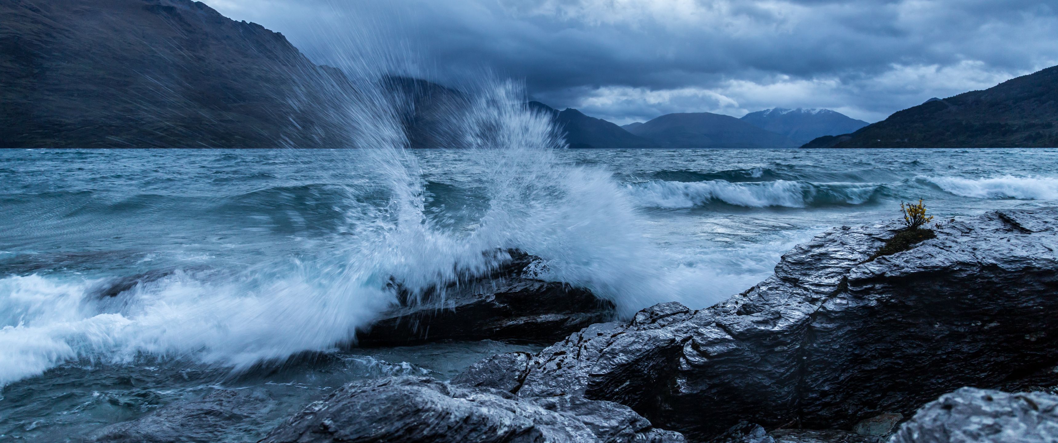A large wave is crashing against the rocks - 3440x1440