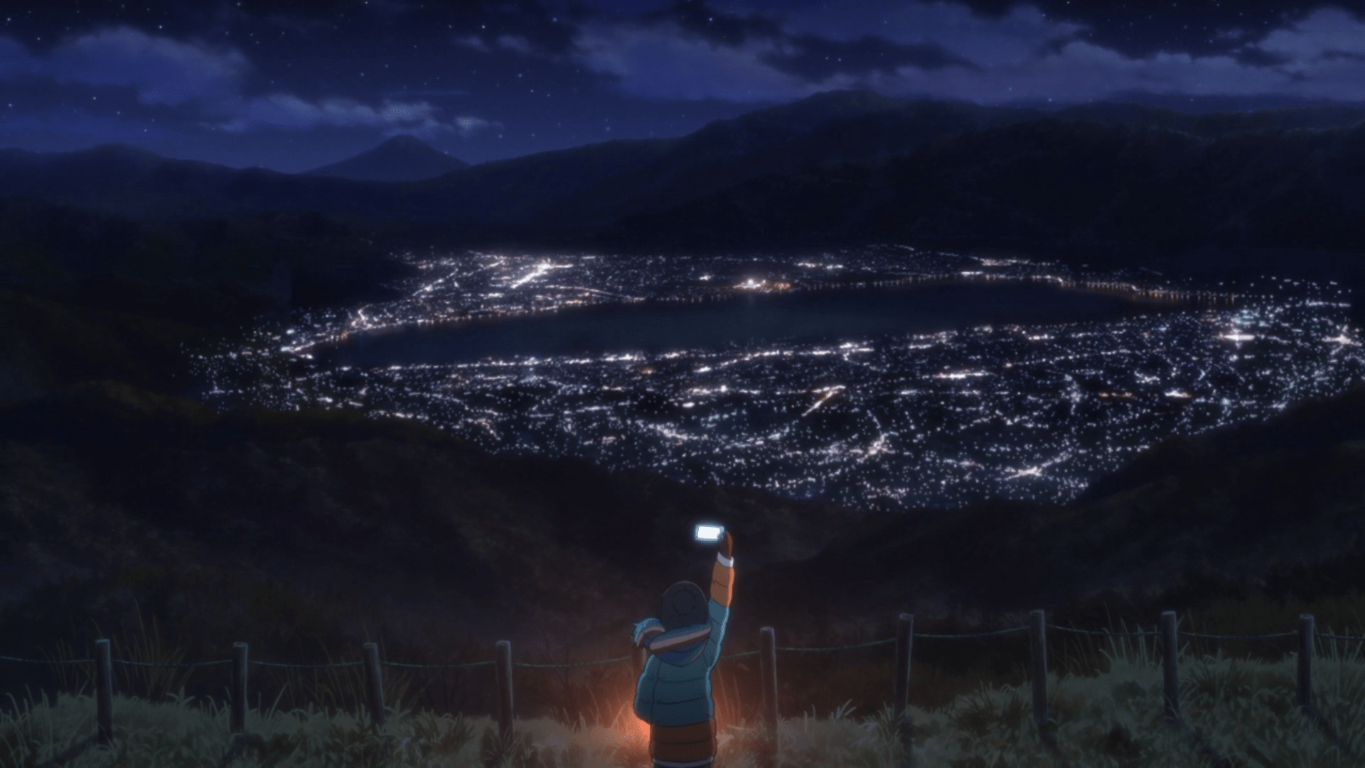 A person holding a cellphone in the air, with a city in the background. - Camping