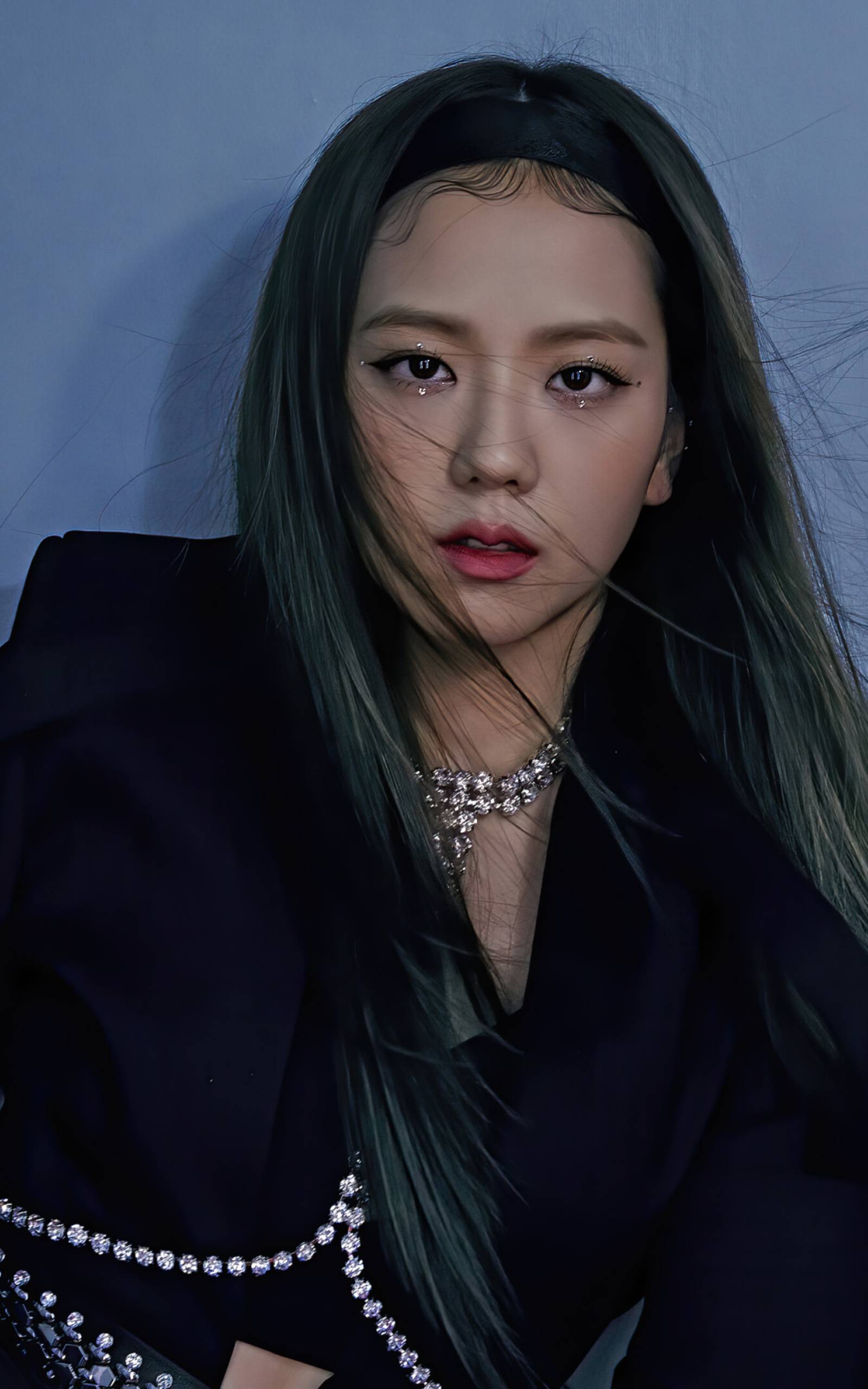 This image features a portrait of BLACKPINK's Rosalia, also known as Jisoo. She is wearing a black blazer and silver necklace. She has long black hair and is looking off to the side. Her makeup is a mix of black and white eyeshadow, with black eyeliner and a pink lip. She is also wearing a black headband. - BLACKPINK