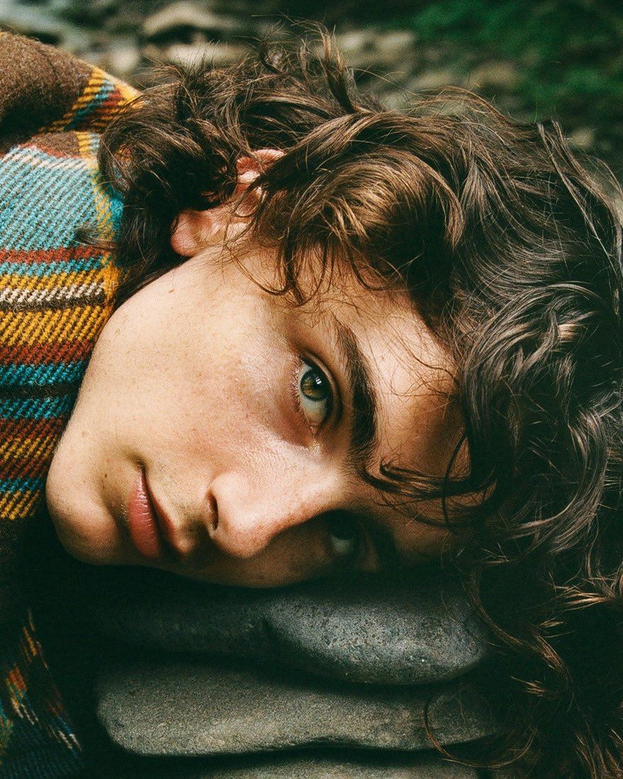 A woman with brown hair and blue eyes laying on a pile of rocks - Timothee Chalamet