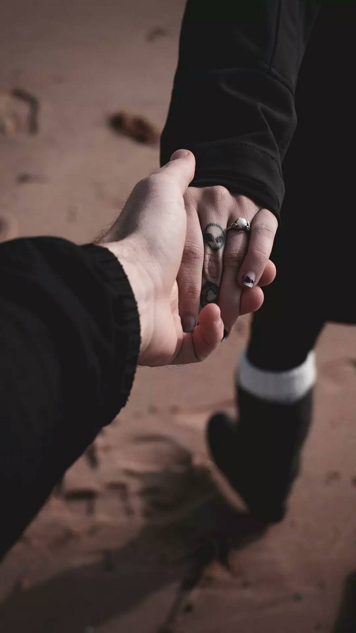 A person holding hands with another in the sand - 