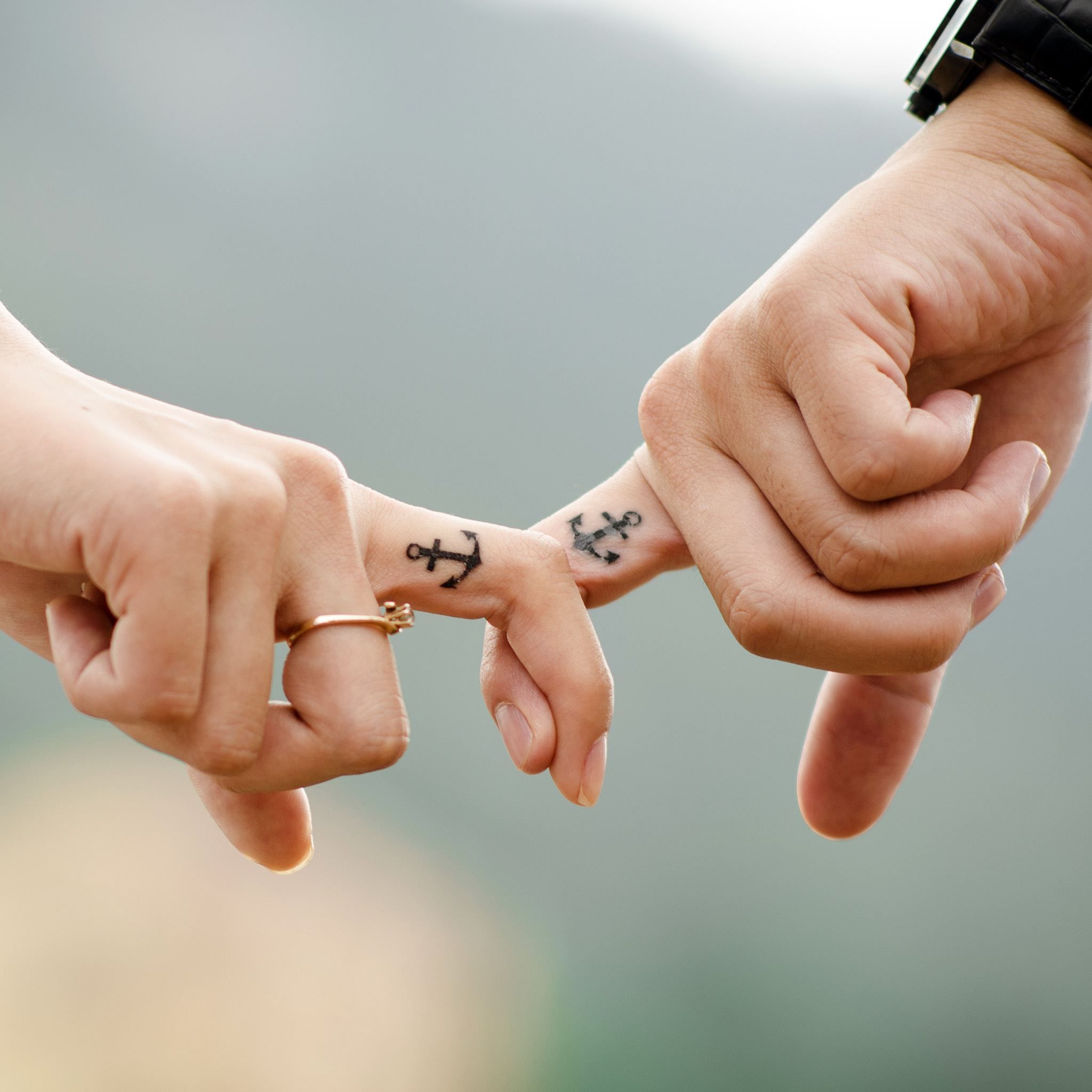 Two people holding hands with tattoos on their fingers - 