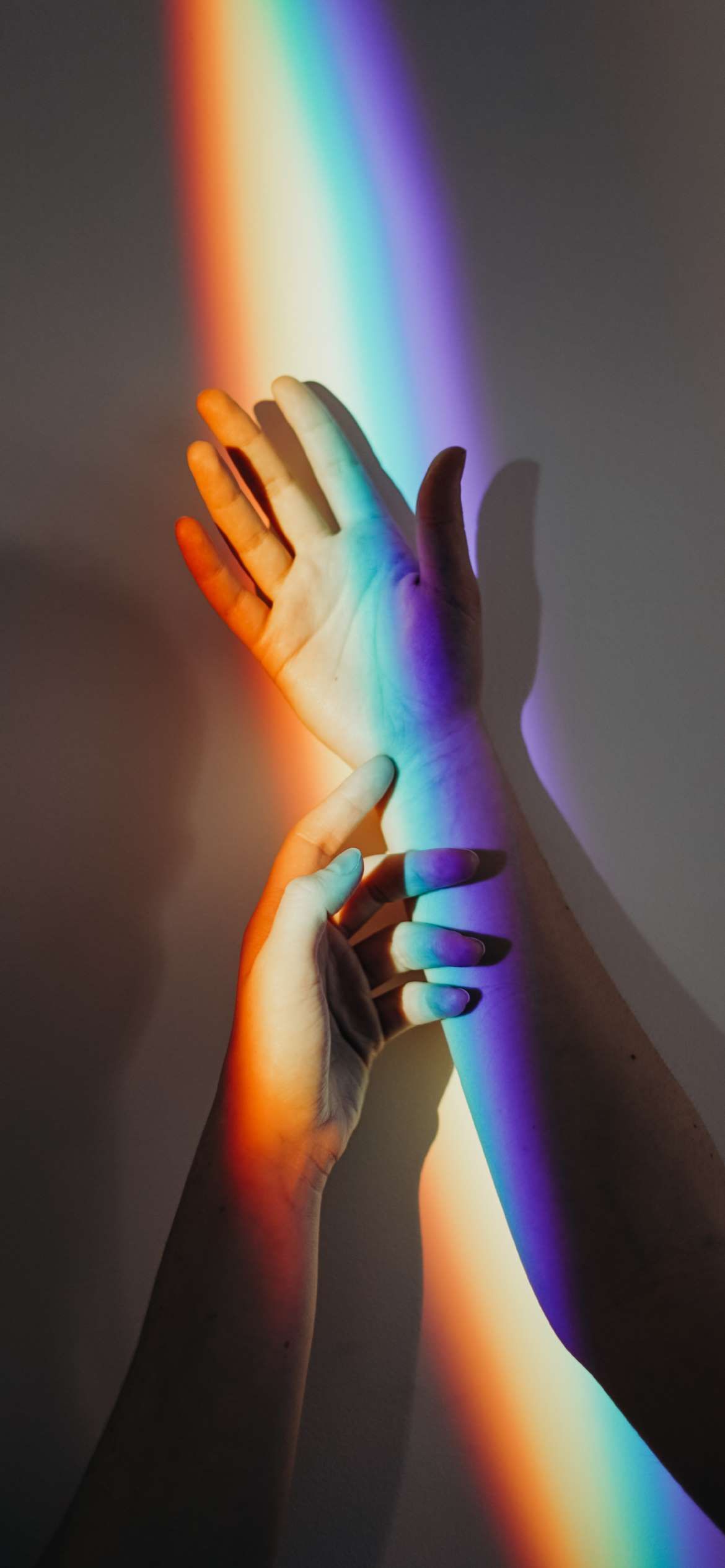 Two hands with rainbow light on them, reaching for each other. - 