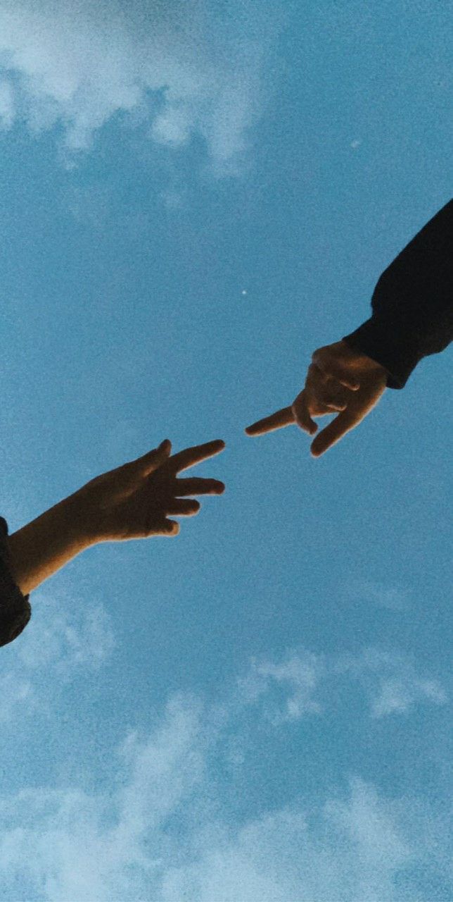 Two hands reaching out to each other against blue sky - 