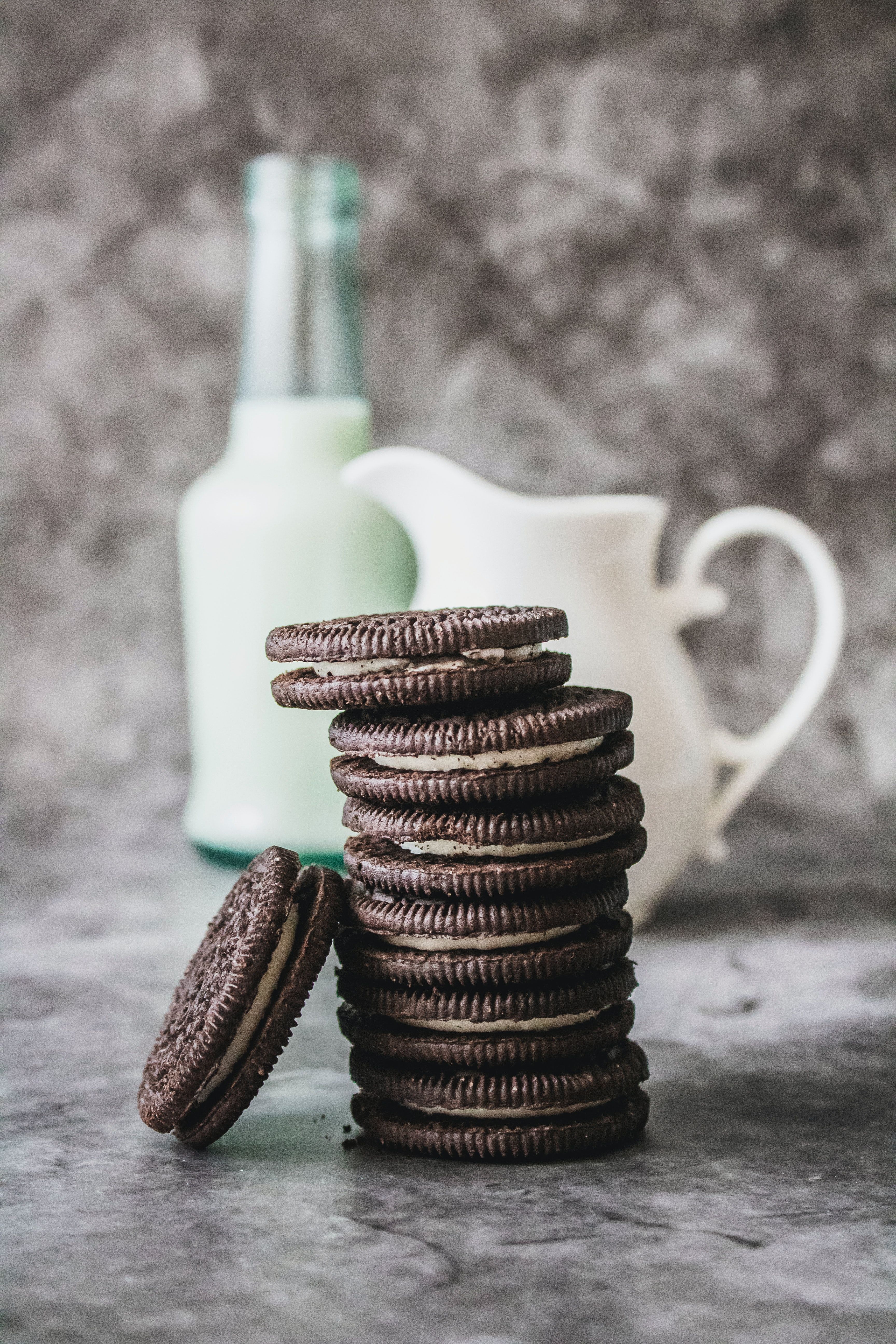 A stack of chocolate sandwich cookies with a bottle of milk in the background. - Oreo