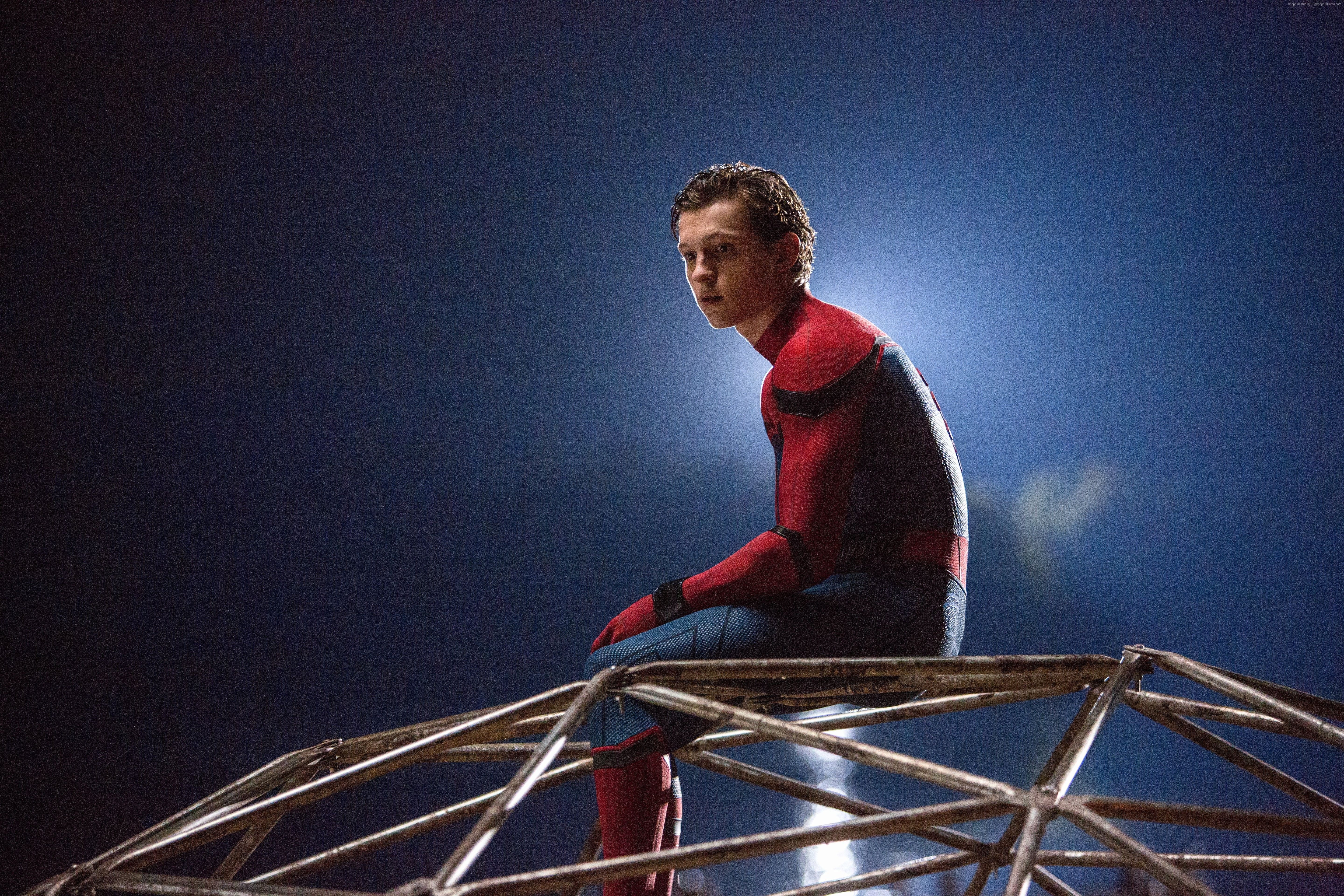 Tom Holland as Spider-Man in Spider-Man: Homecoming. He's sitting on a metal structure, wearing his Spider-Man suit, with a blue background. - Marvel, Tom Holland