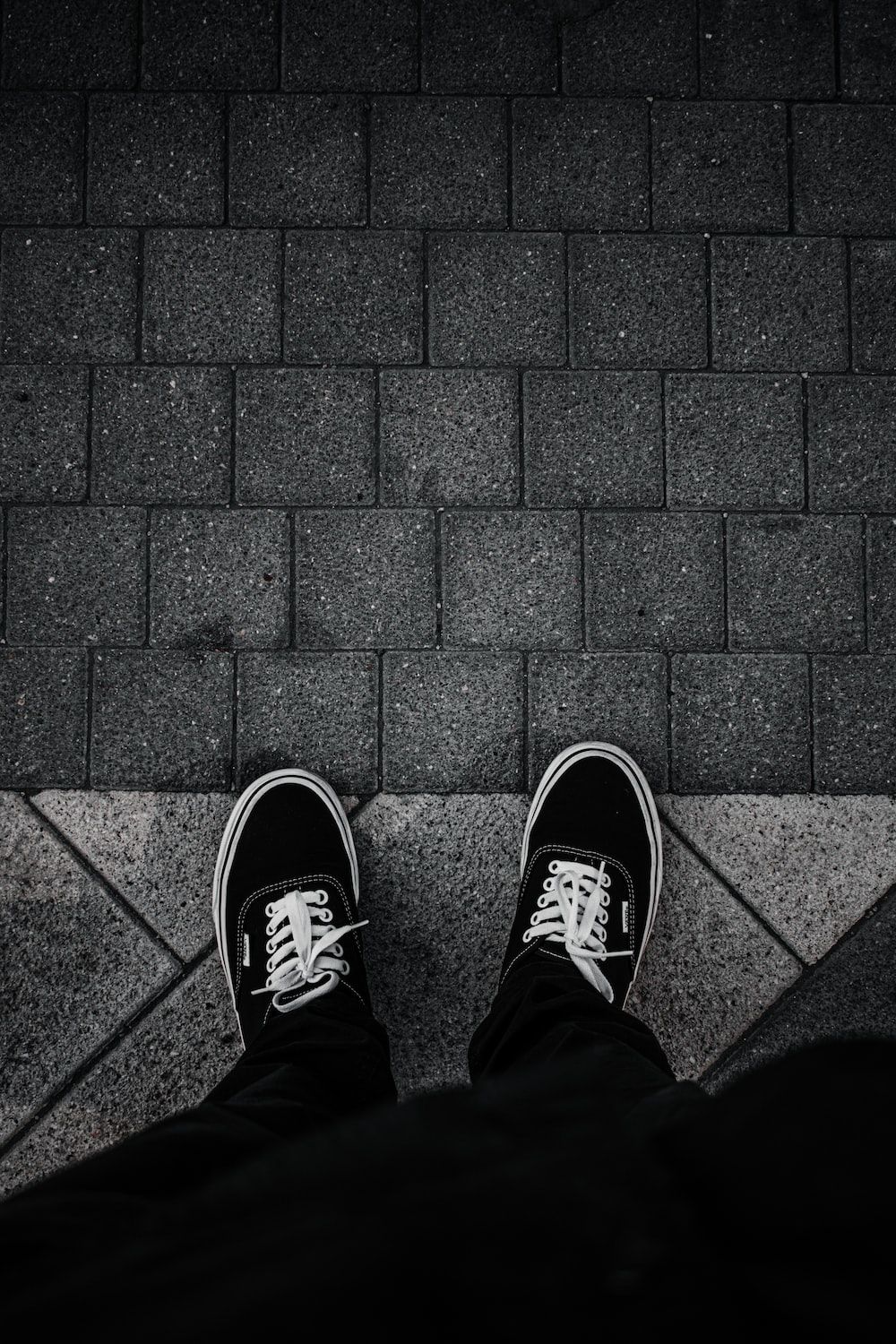 Person wearing black and white Vans sneakers standing on the sidewalk - Shoes, Vans