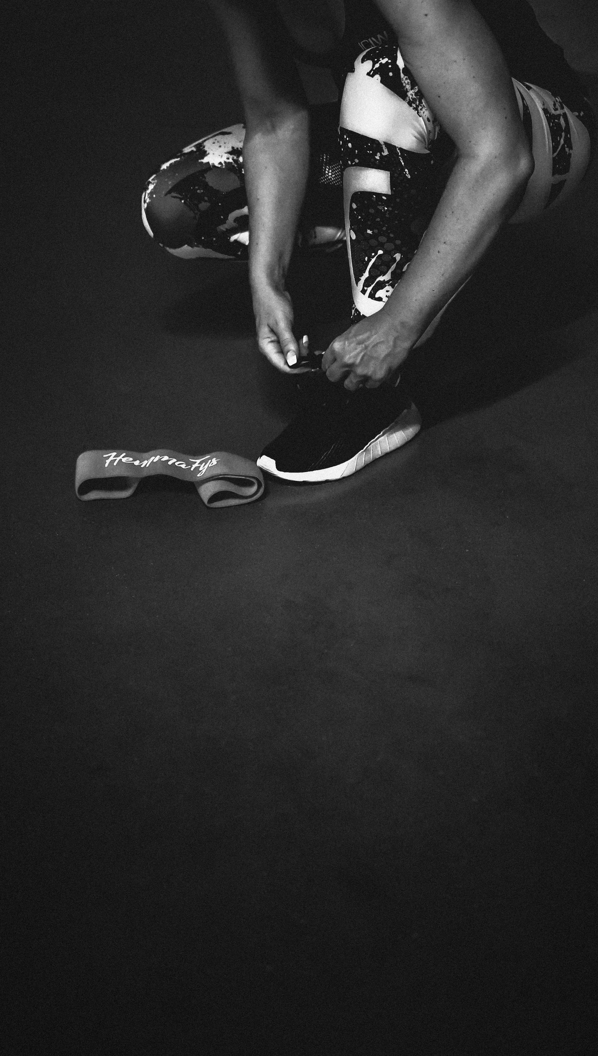 A woman is kneeling down and tying her shoes - Shoes, gym