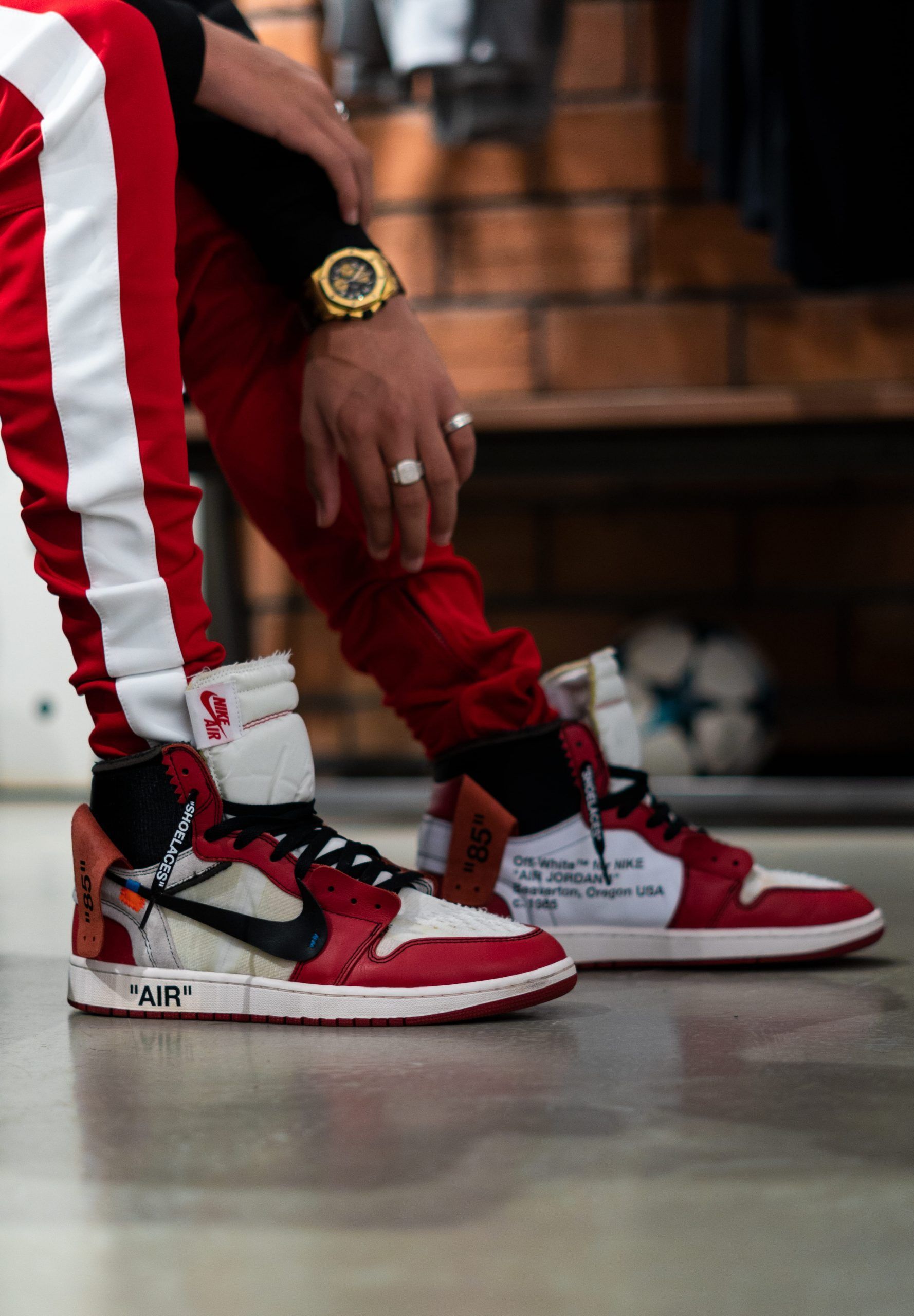 A person in red and white pants standing next to a pair of sneakers. - Shoes, Air Jordan 1, Off-White, Air Jordan