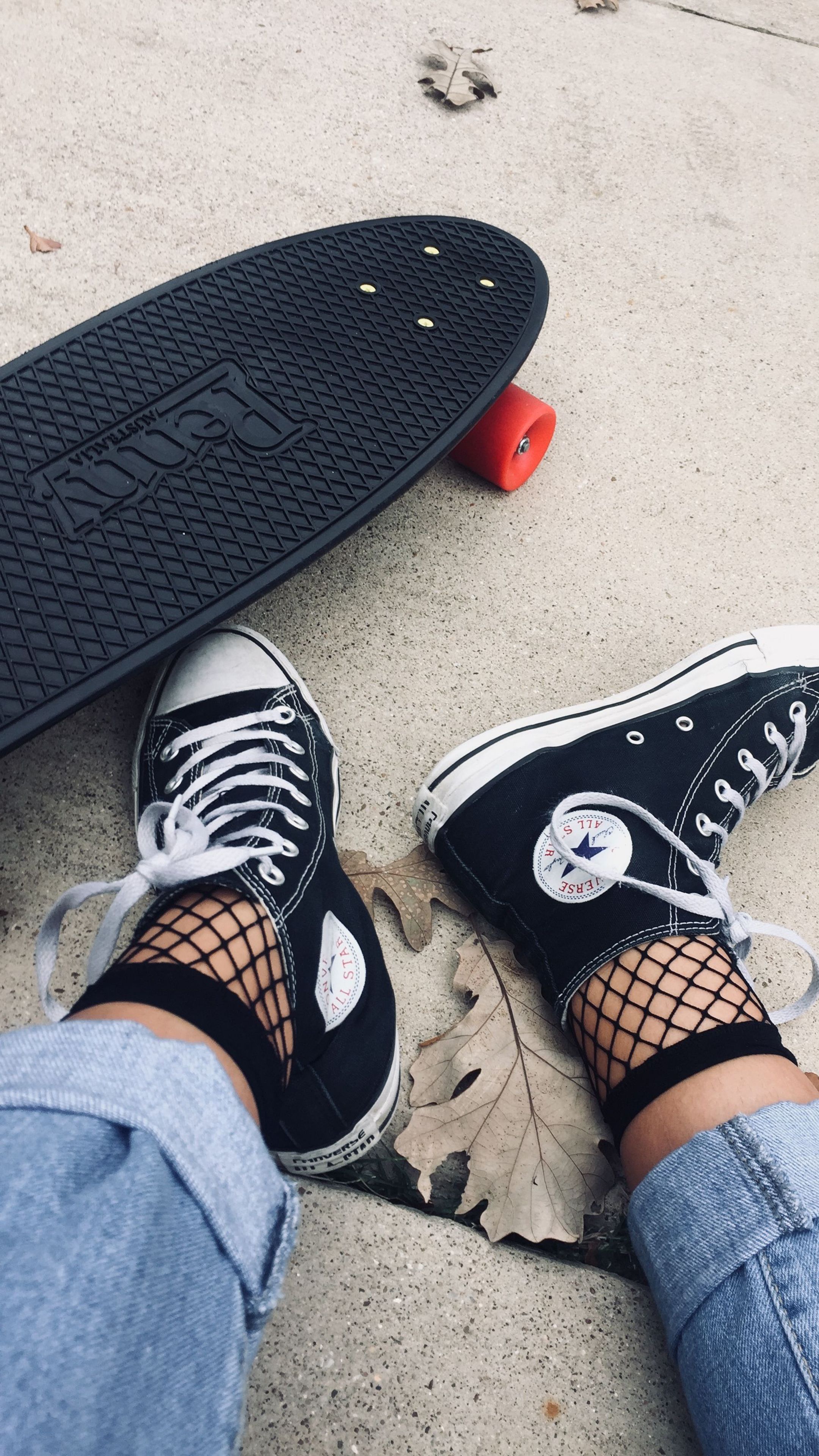 A girl wearing fishnet socks and converse sneakers standing next to a skateboard - Shoes
