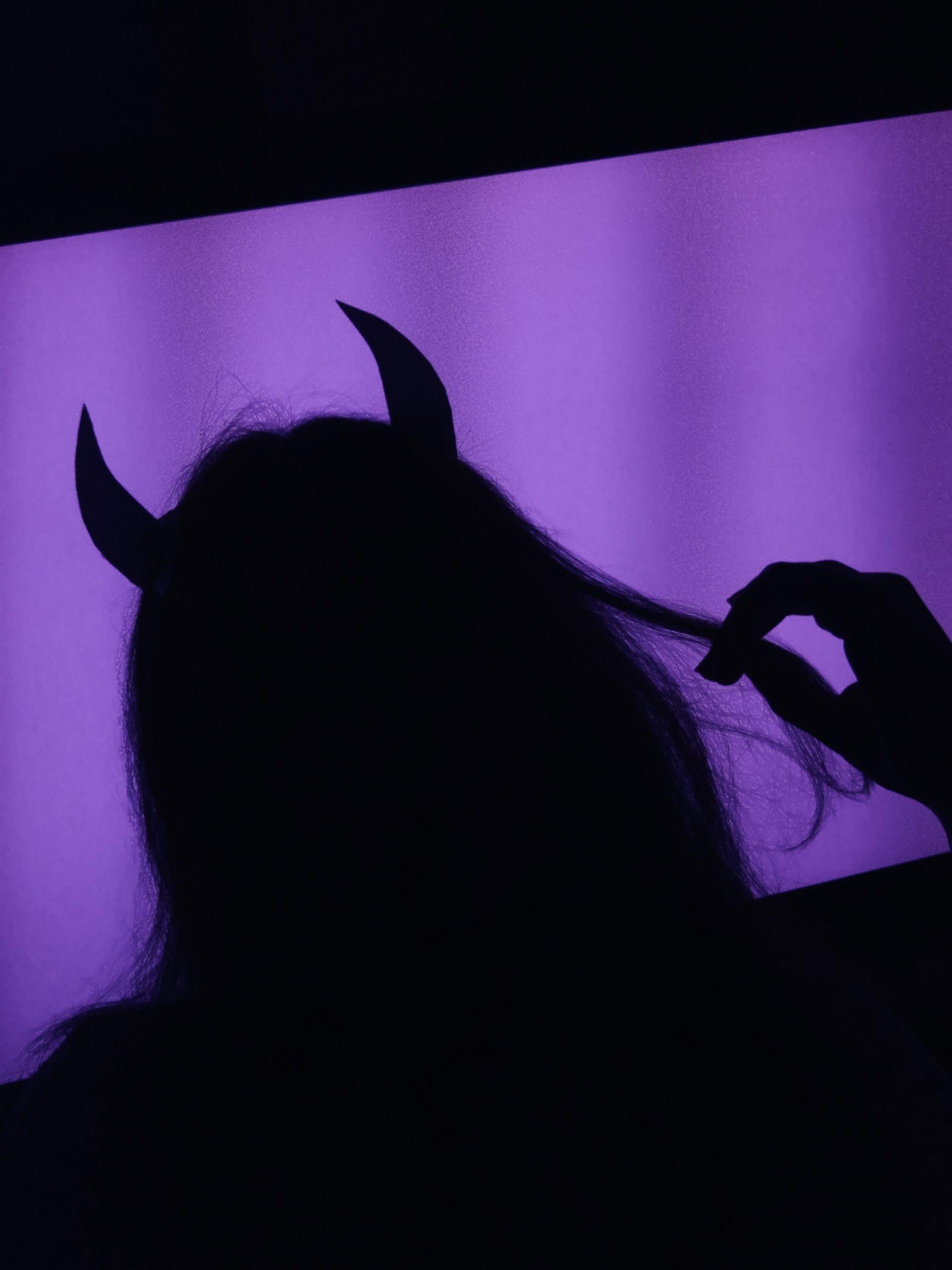 A woman with horns on her head and a purple background - Dark purple, shadow