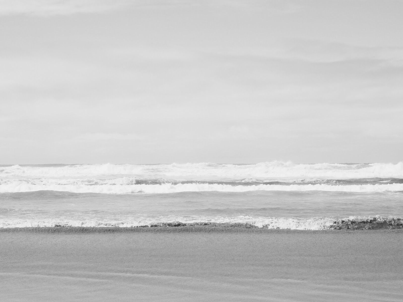 A black and white photo of a sandy beach with crashing waves - Gray