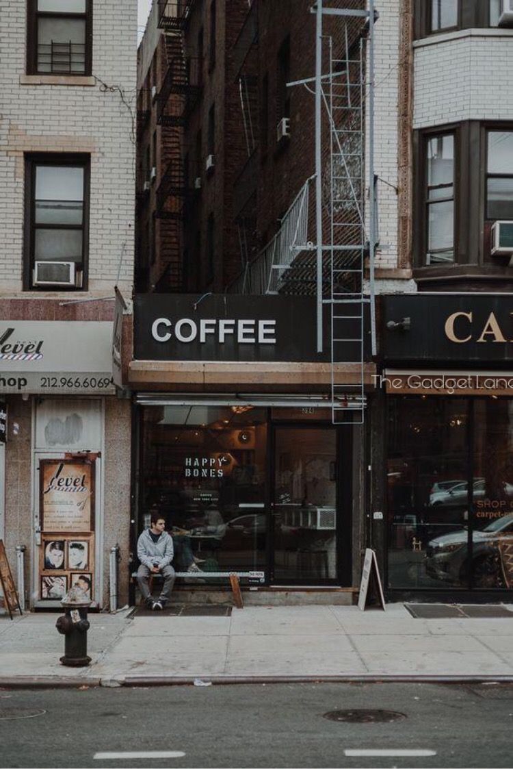 A man sitting on the sidewalk in front of coffee shop - New York