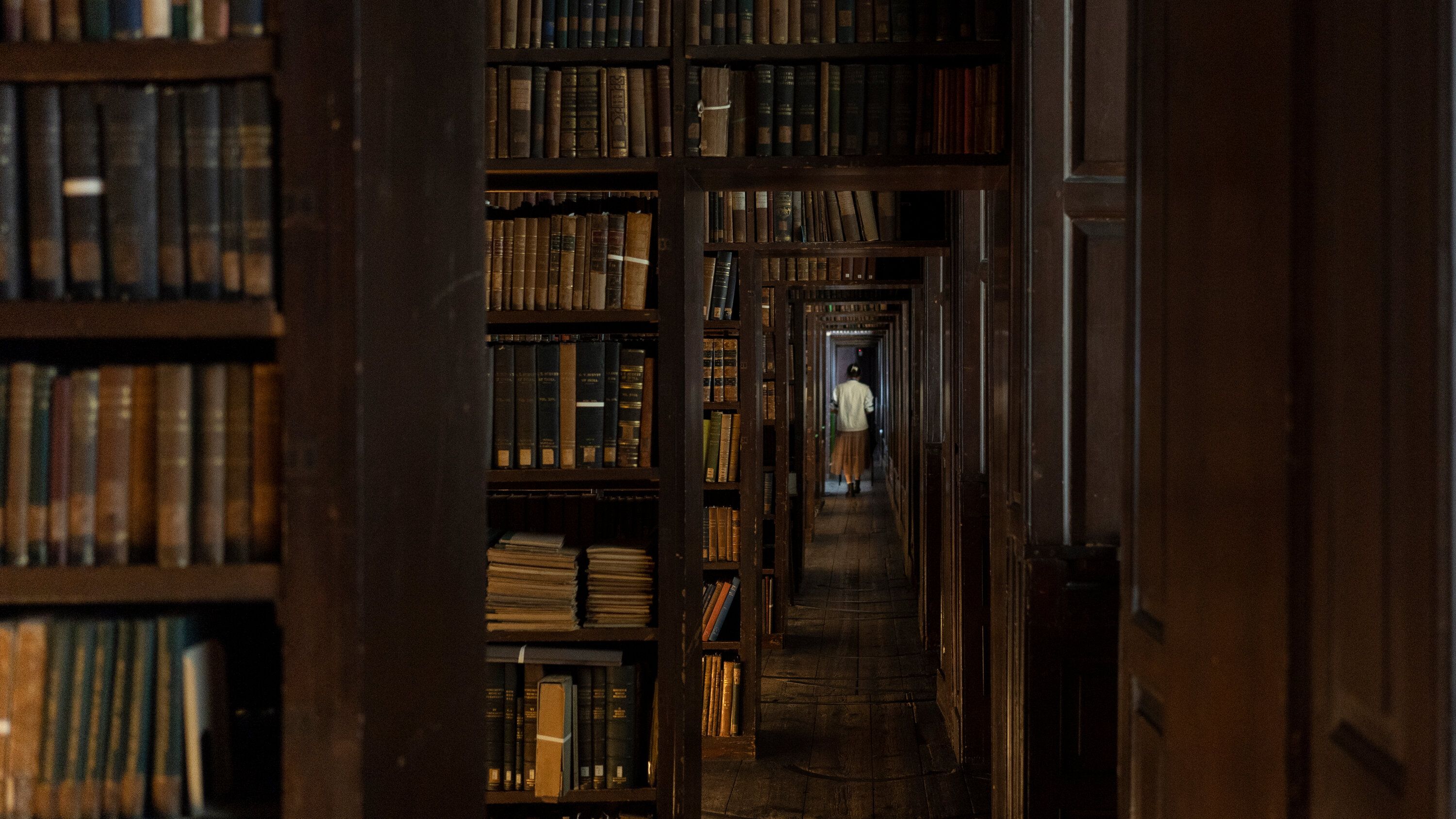 A person standing in a dimly lit library surrounded by book shelves - Dark academia