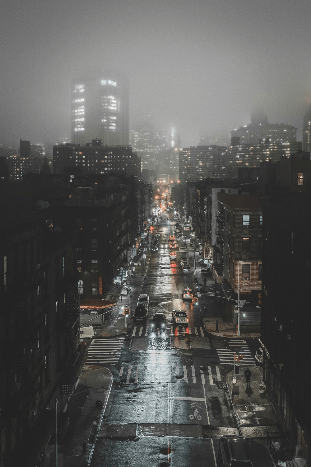 A street in the city at night with cars and pedestrians. - Fog