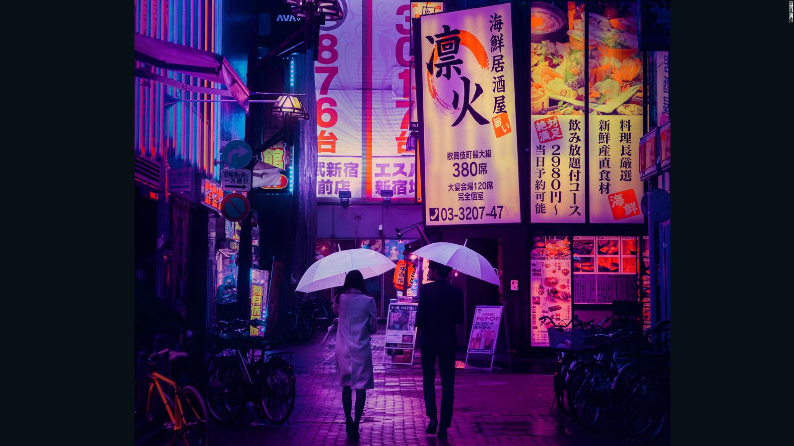 A couple walks under umbrellas in a Tokyo street at night. - Tokyo