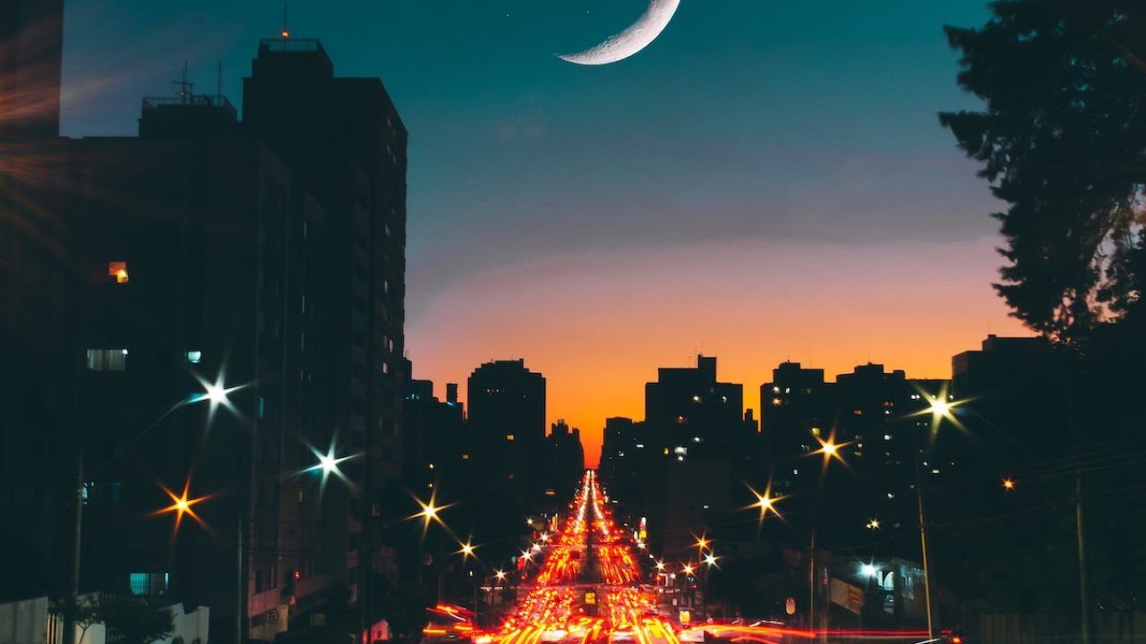 A city street at night with the moon in view - Chromebook