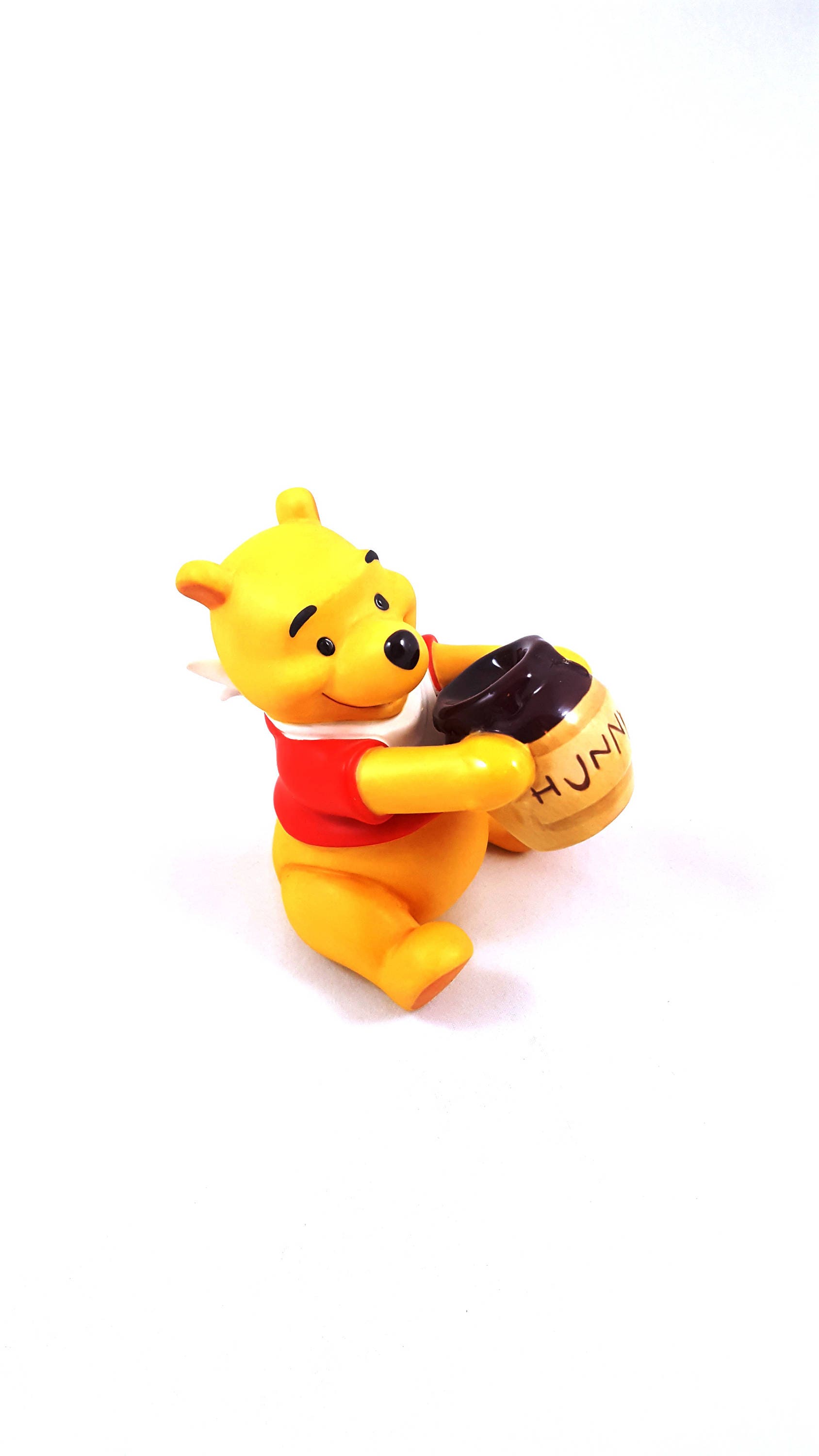 A Winnie the Pooh figurine holding a small basket with the word Hunny on it. - Winnie the Pooh