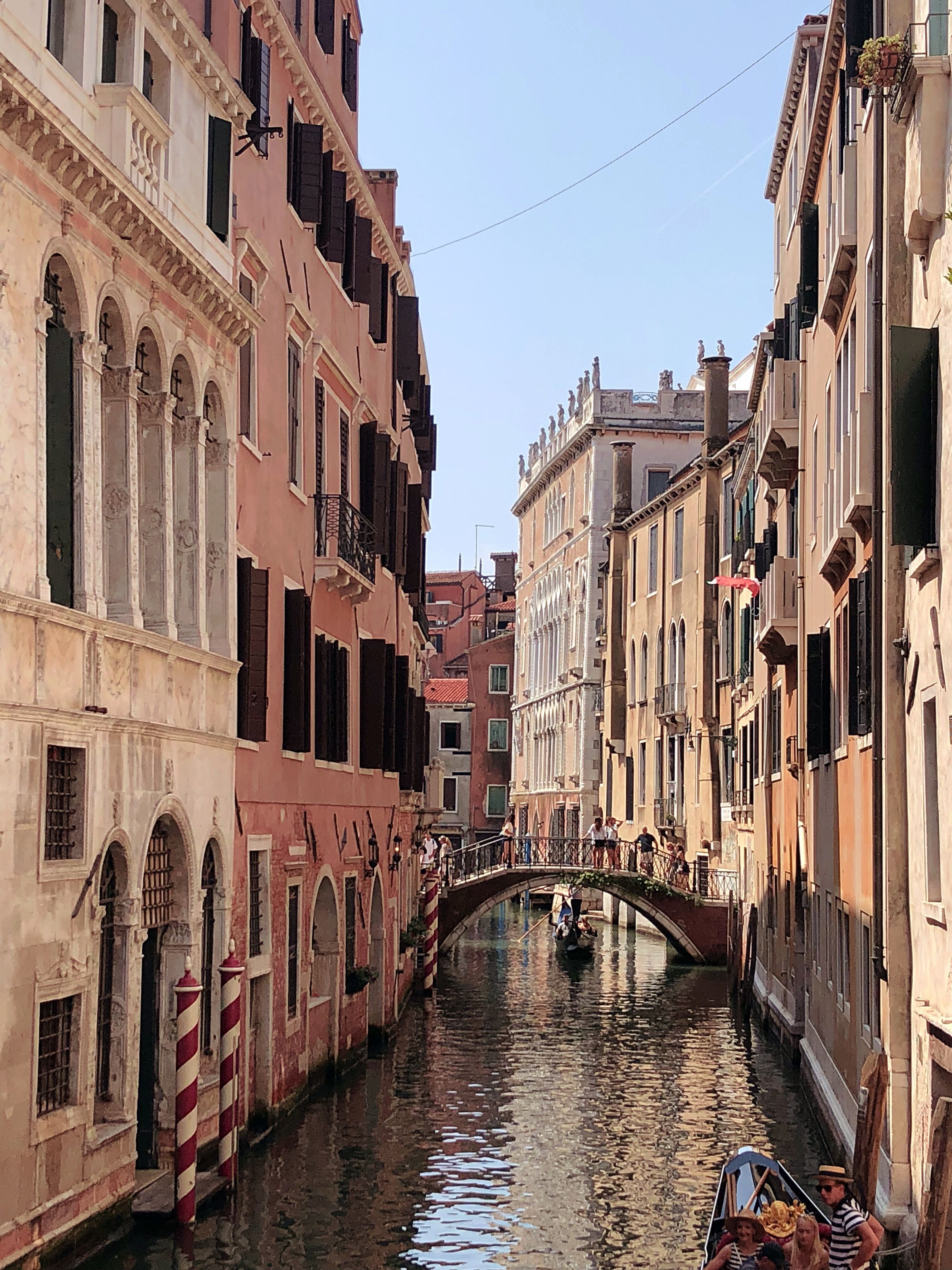 A view of a canal in Venice, Italy with buildings on either side and a bridge in the distance. - Italy