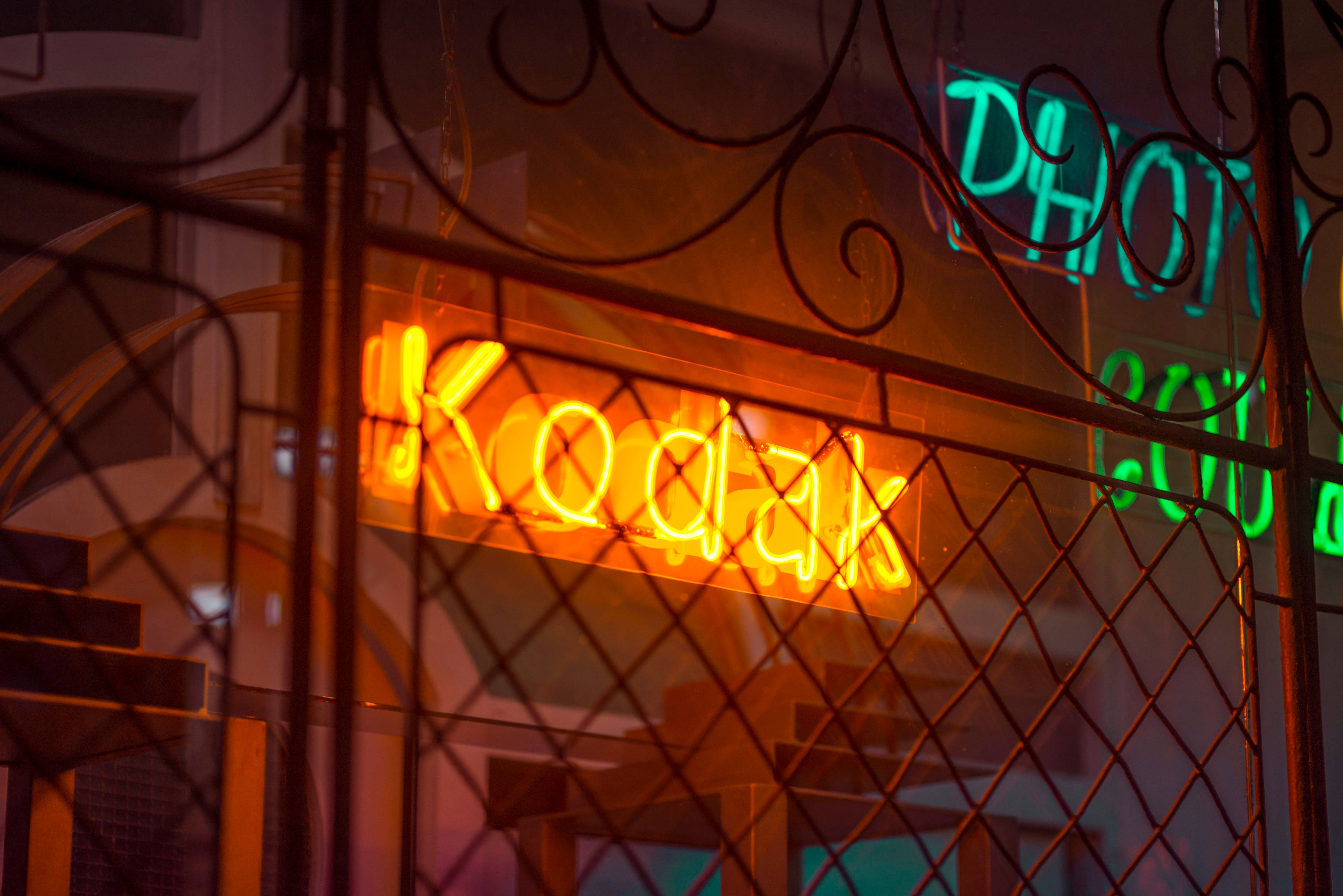 A neon sign that says Kodak in yellow and green letters. - Neon orange