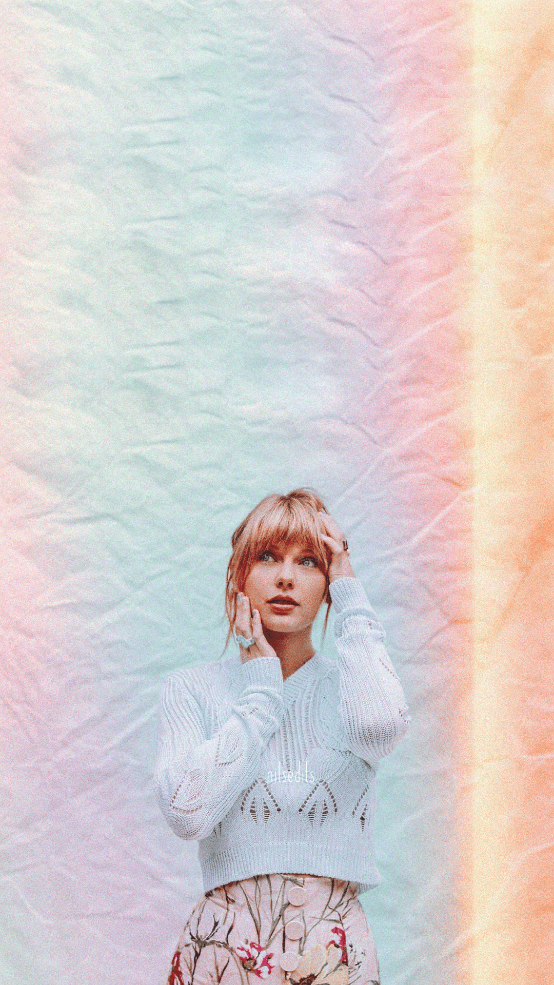 A woman with her hands in her hair standing in front of a rainbow background - Taylor Swift