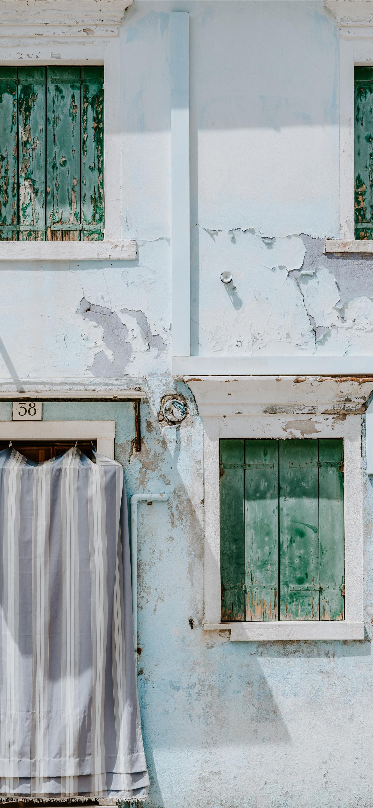 A close up of a building with green shutters and a striped cloth hanging out to dry - Pastel blue