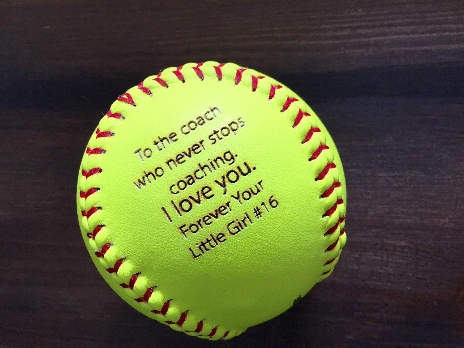 A yellow baseball with writing on it - Softball