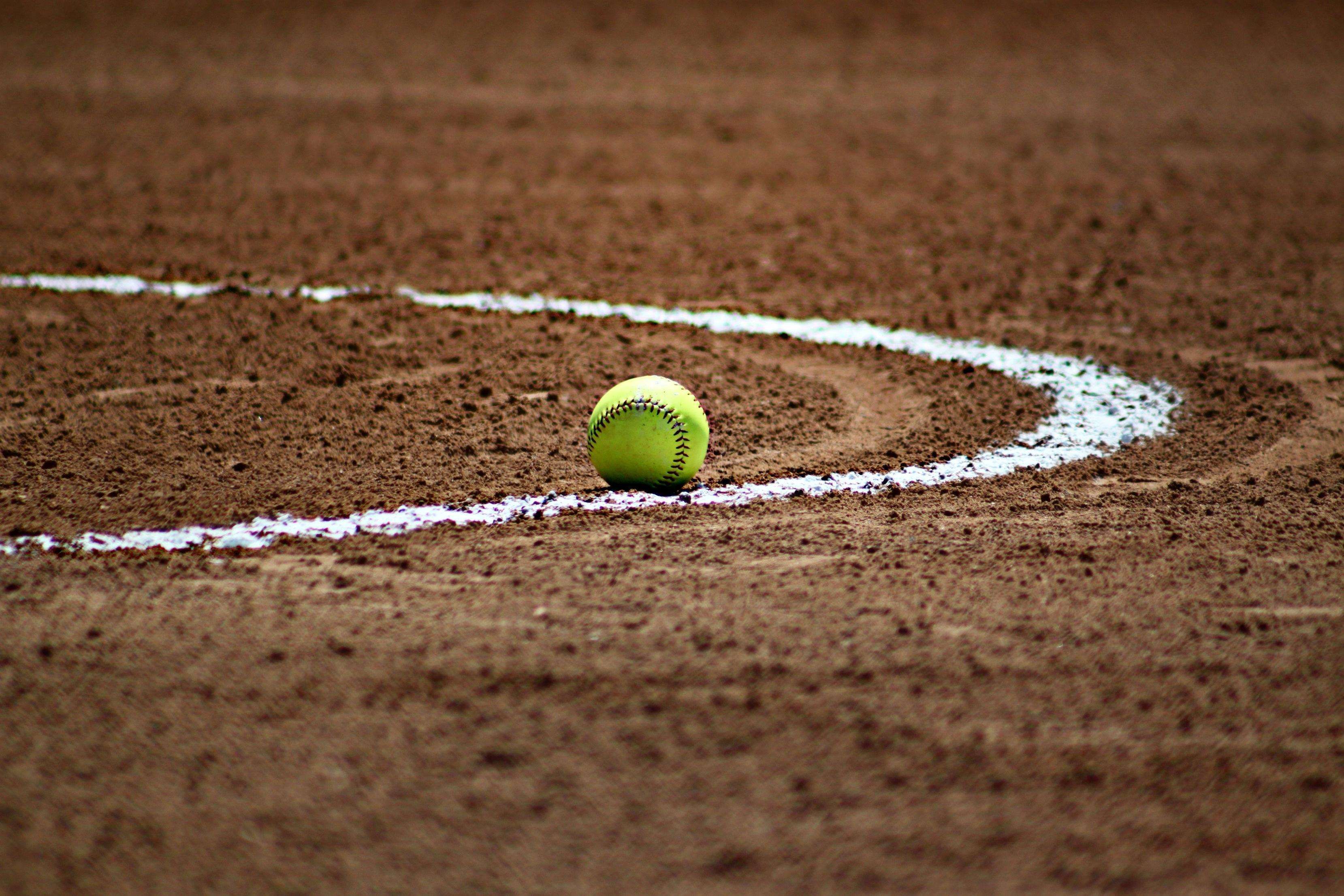 A yellow softball sitting on the ground - Softball