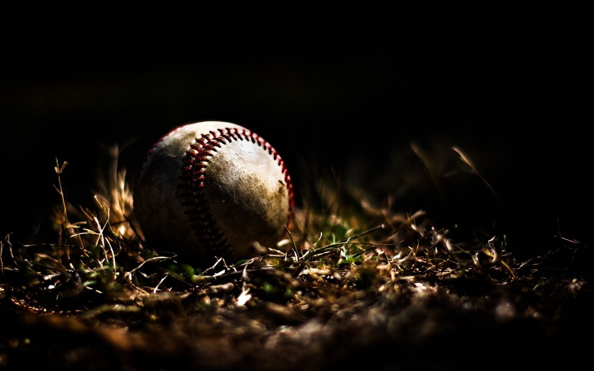 A baseball sitting in the grass on top of dirt - Softball