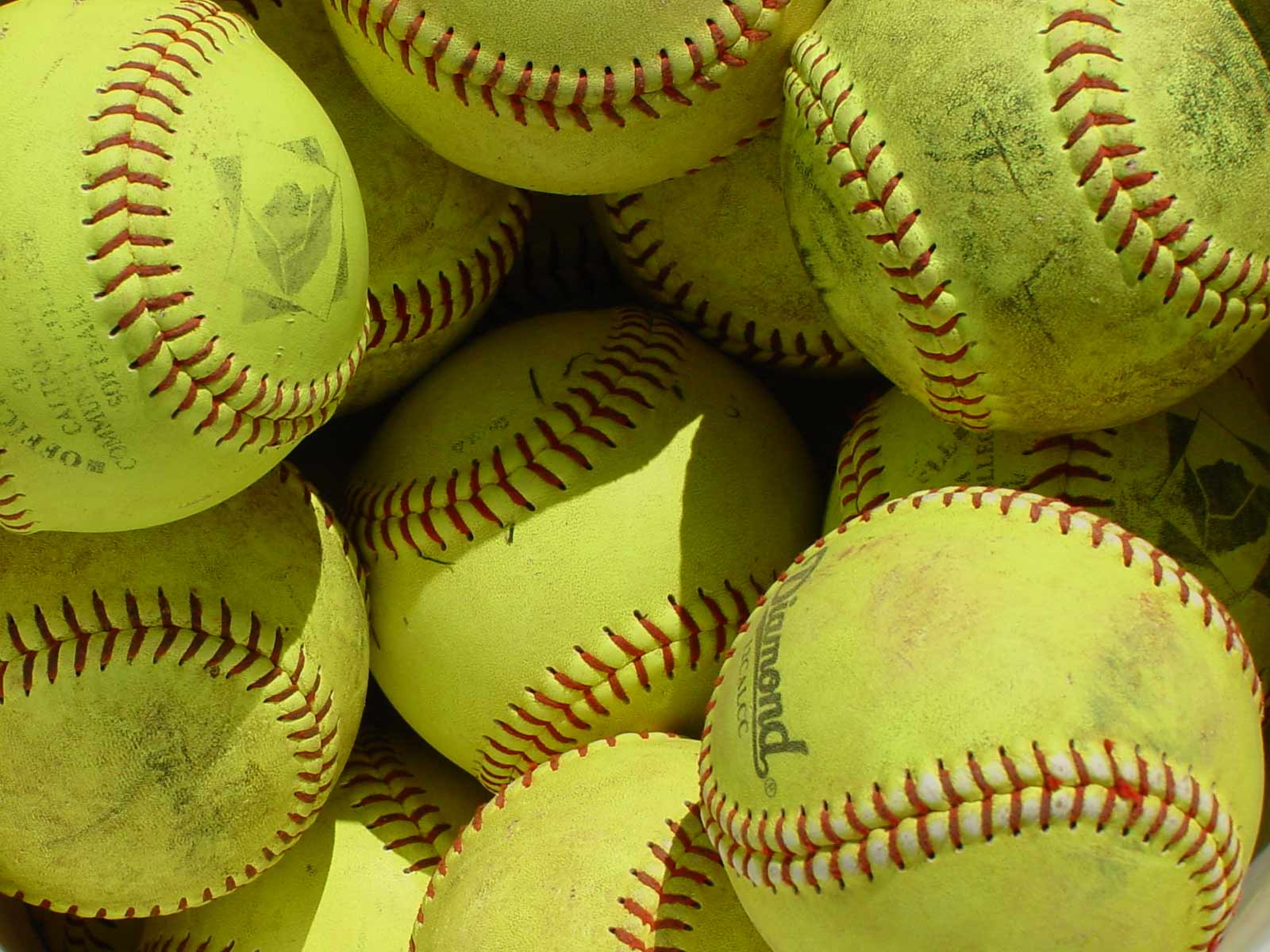 A pile of yellow baseballs with red stitching. - Softball