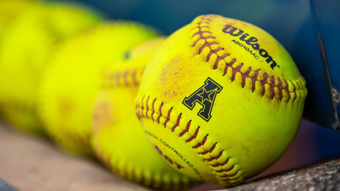 Softballs sit in the dugout before a game. - Softball