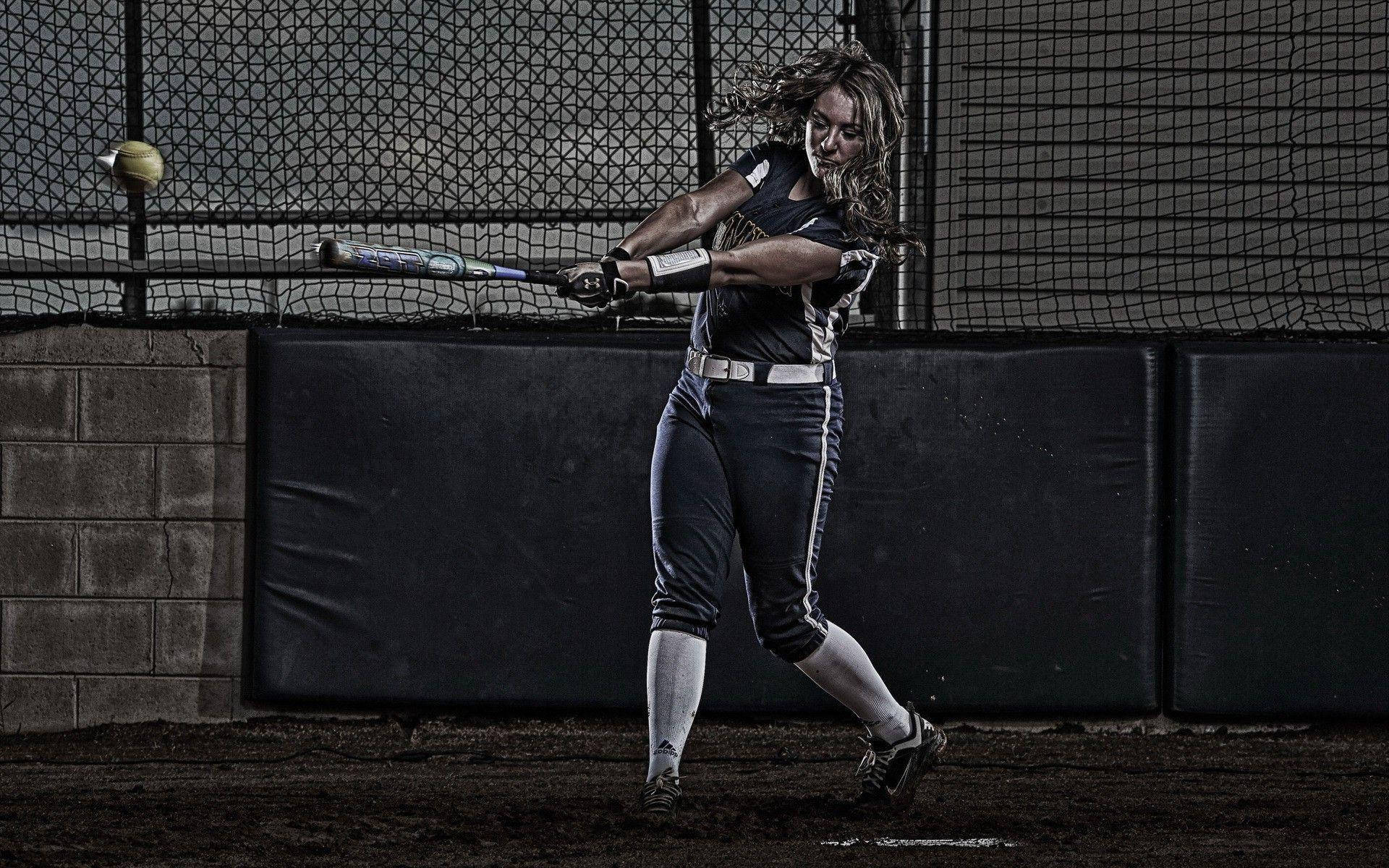 A woman swinging a baseball bat at a ball. - Softball