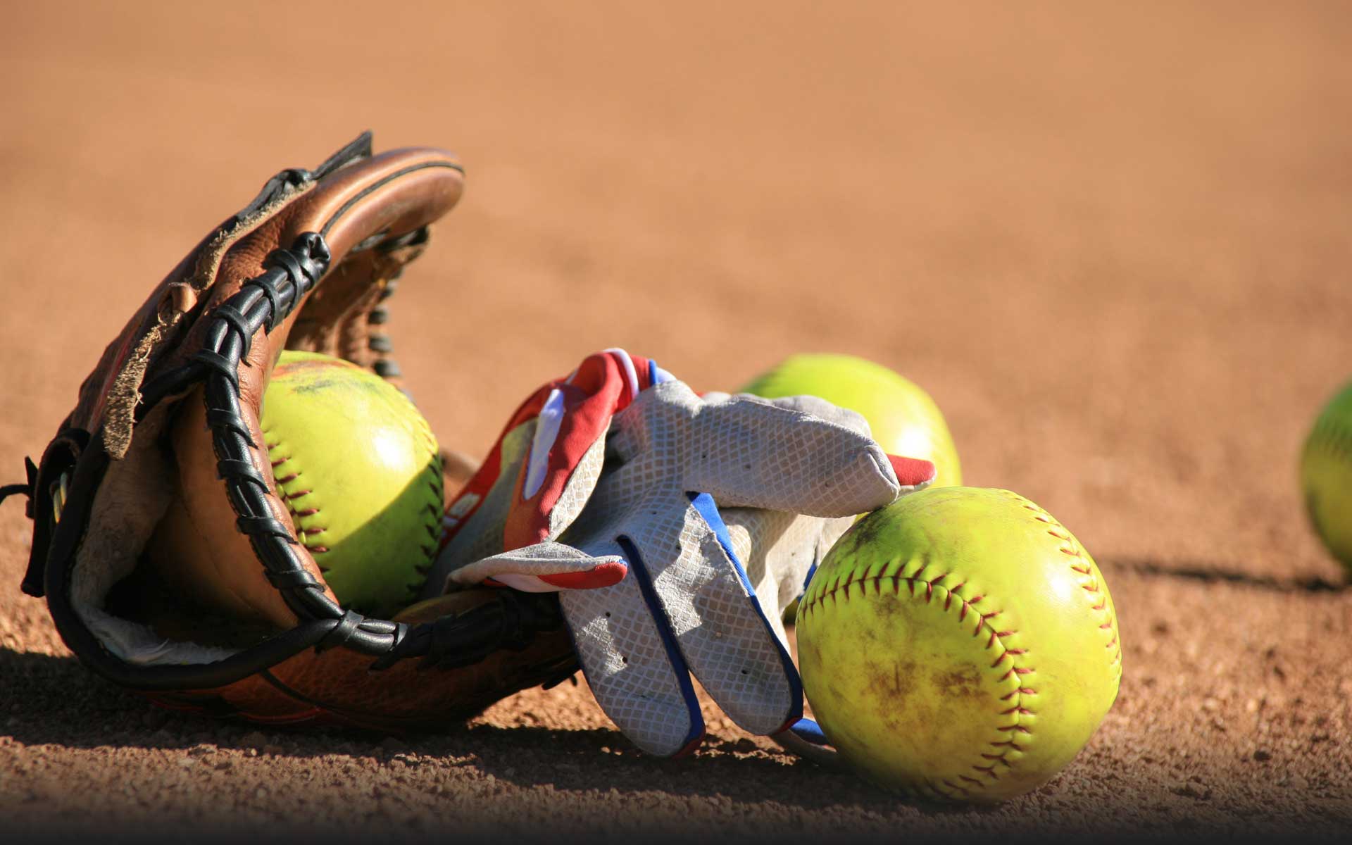 A baseball glove and some softballs on the ground - Softball