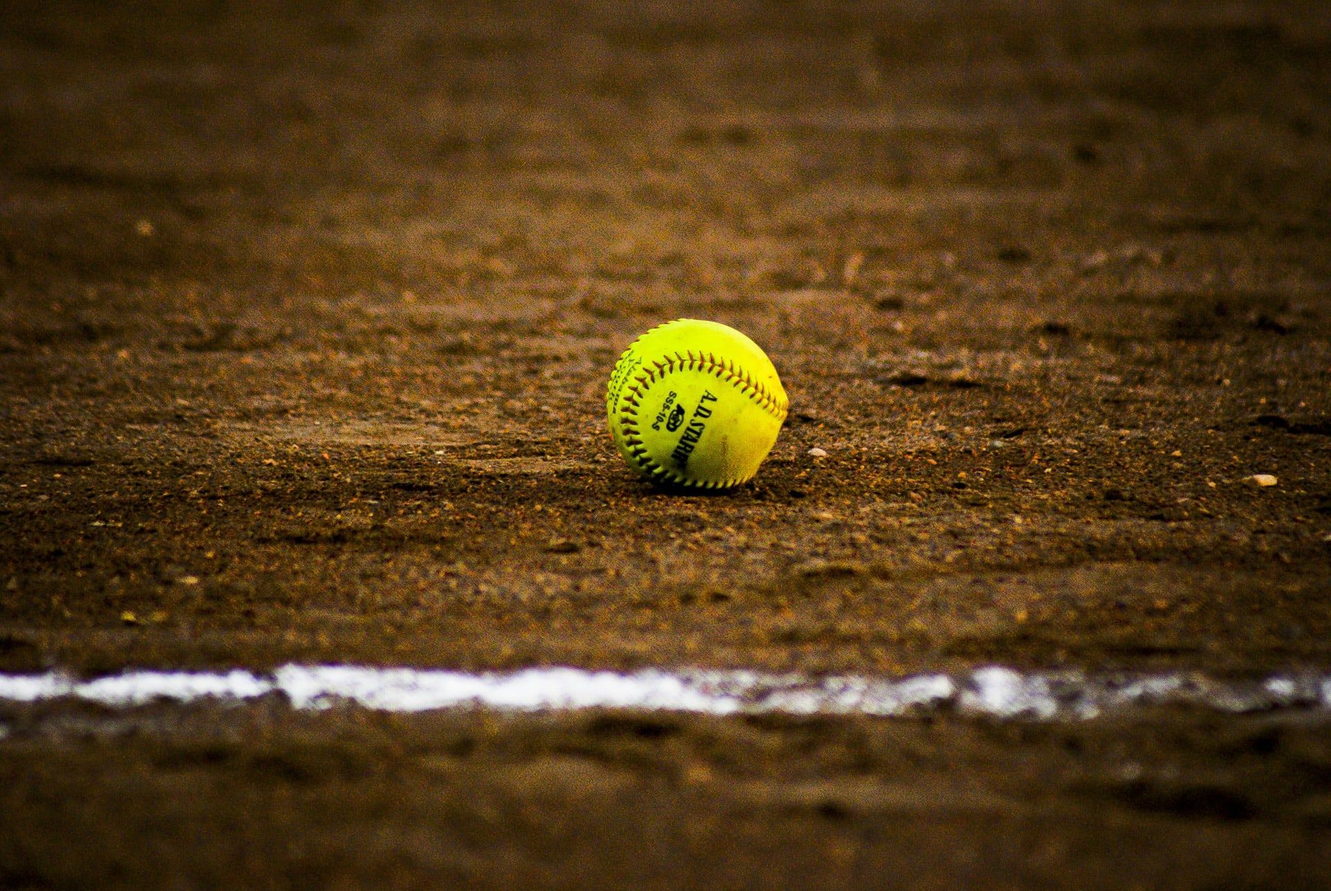 A softball sitting on the ground in front of some dirt - Softball