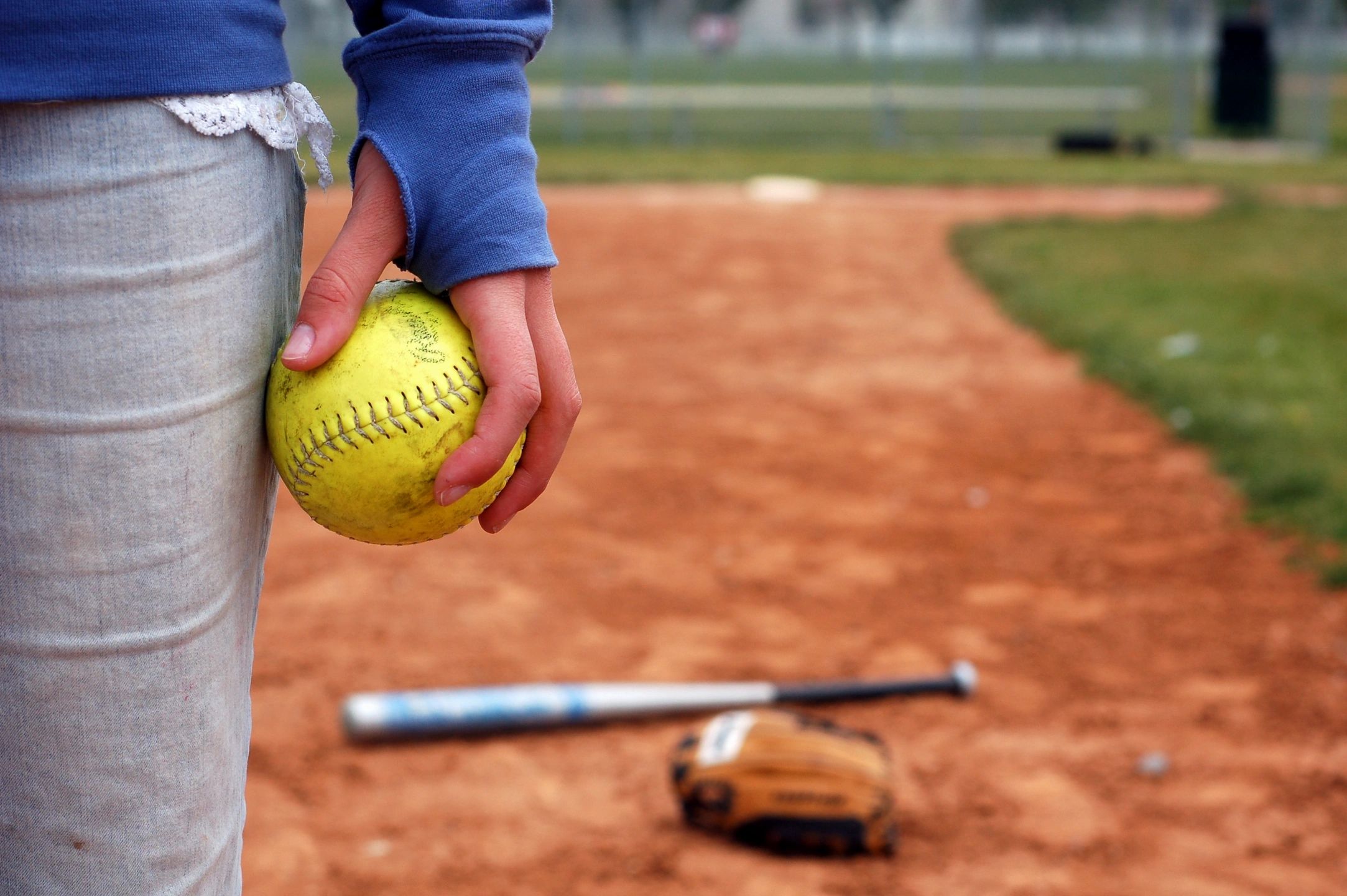 A woman in white pants is holding a yellow softball. - Softball