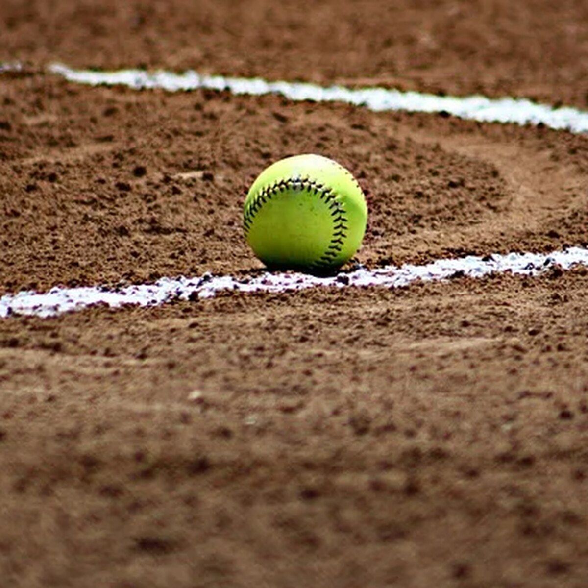 A softball sitting on the ground next to some white lines - Softball