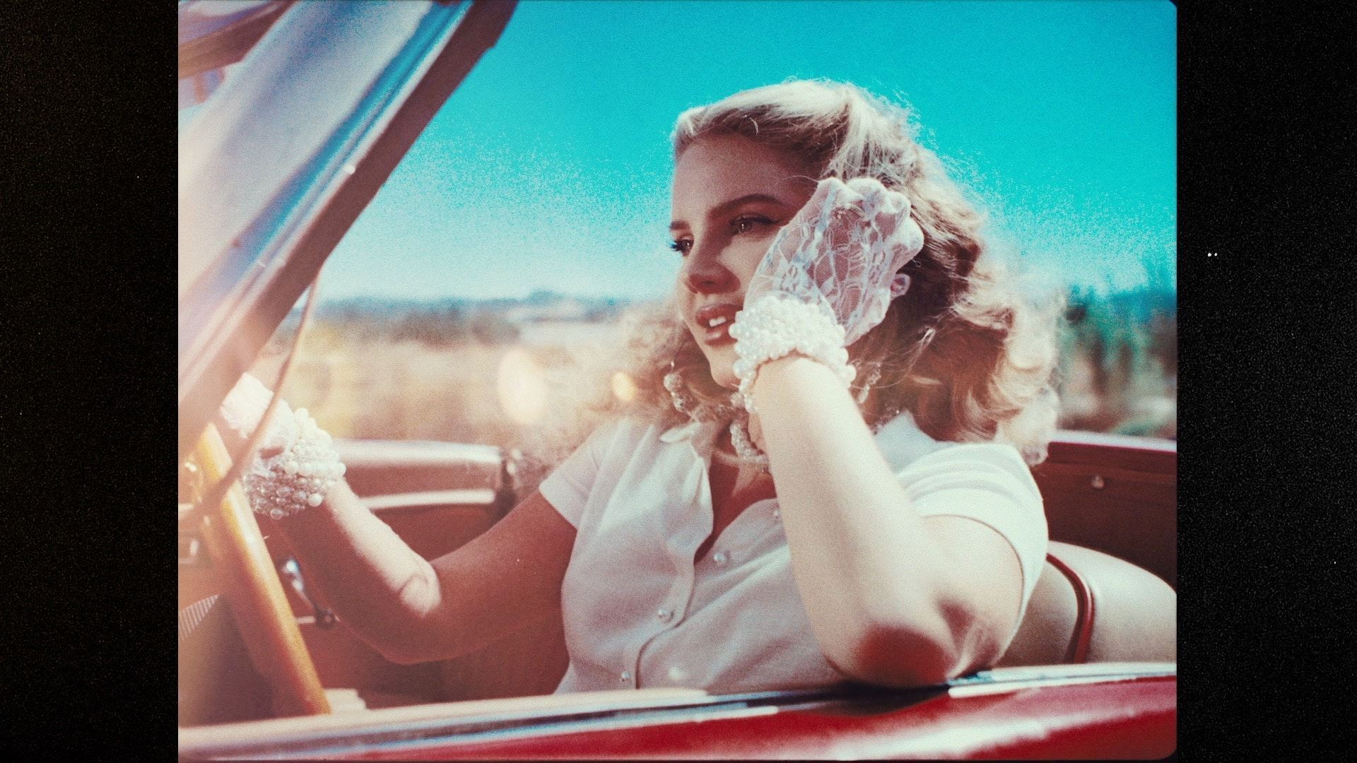 A woman in a convertible car, wearing a white lace glove on her left hand. - Lana Del Rey