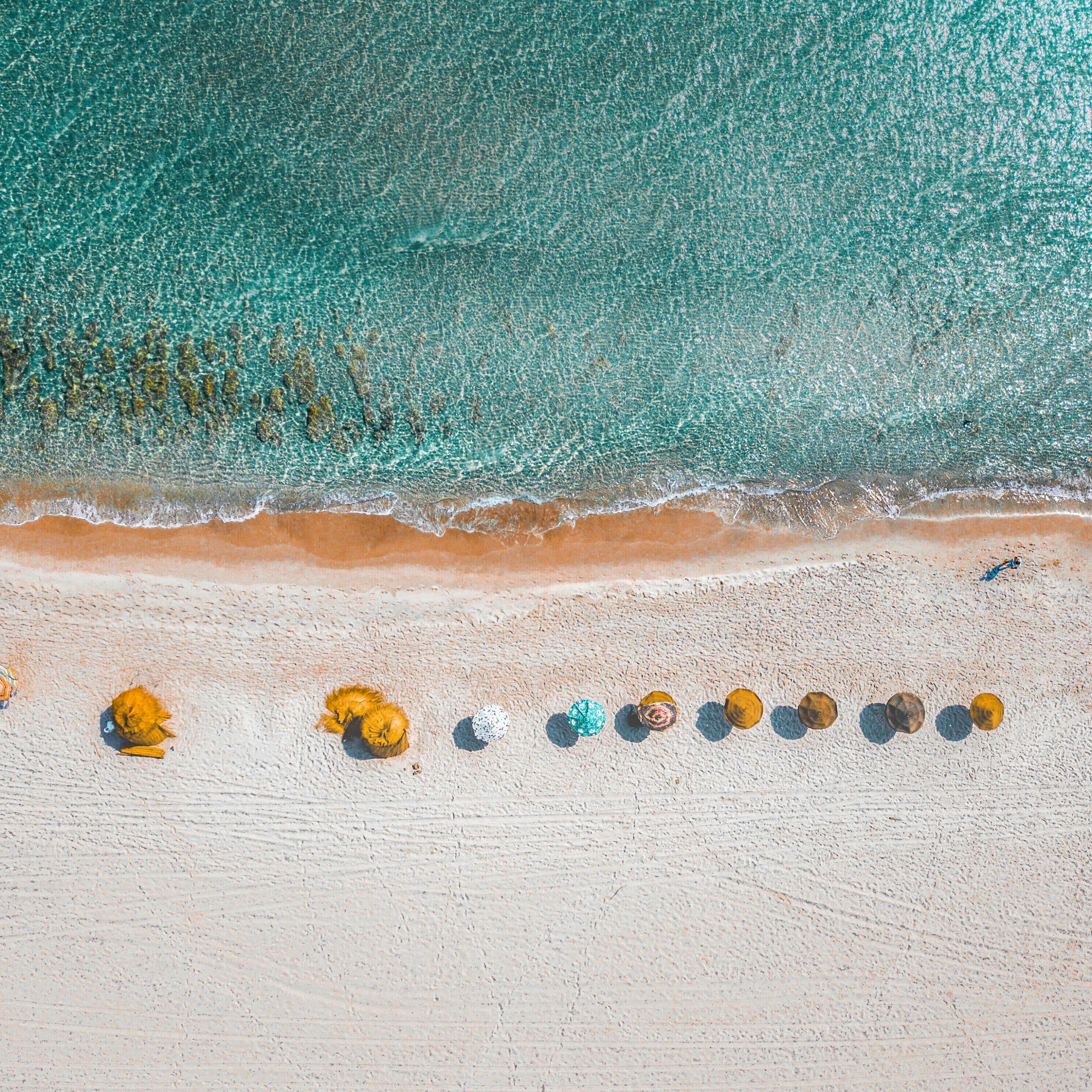 Aerial view of a white sand beach with a row of beach umbrellas and lounge chairs. - Beach, summer
