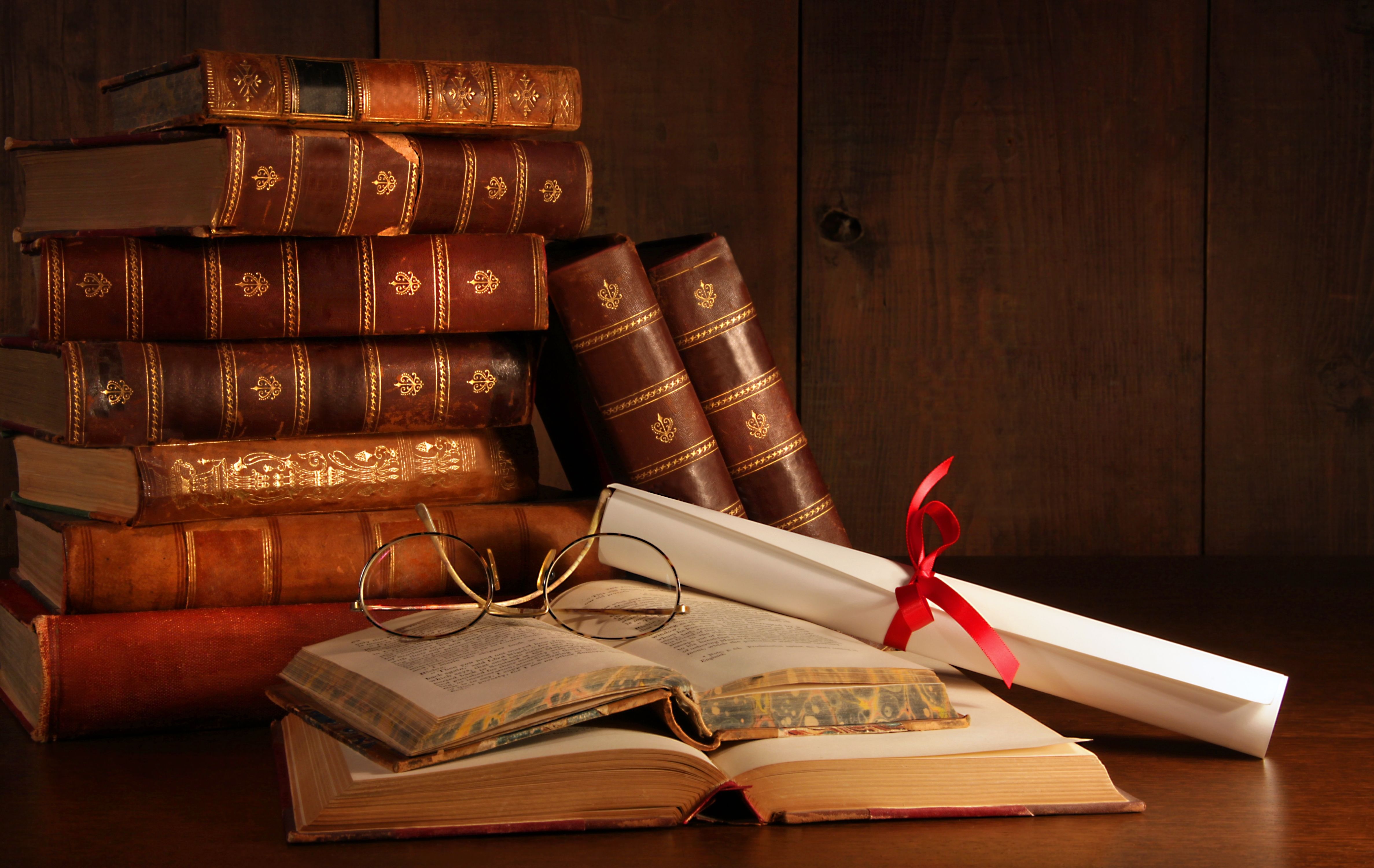 A stack of old books with a diploma and glasses on top. - Books