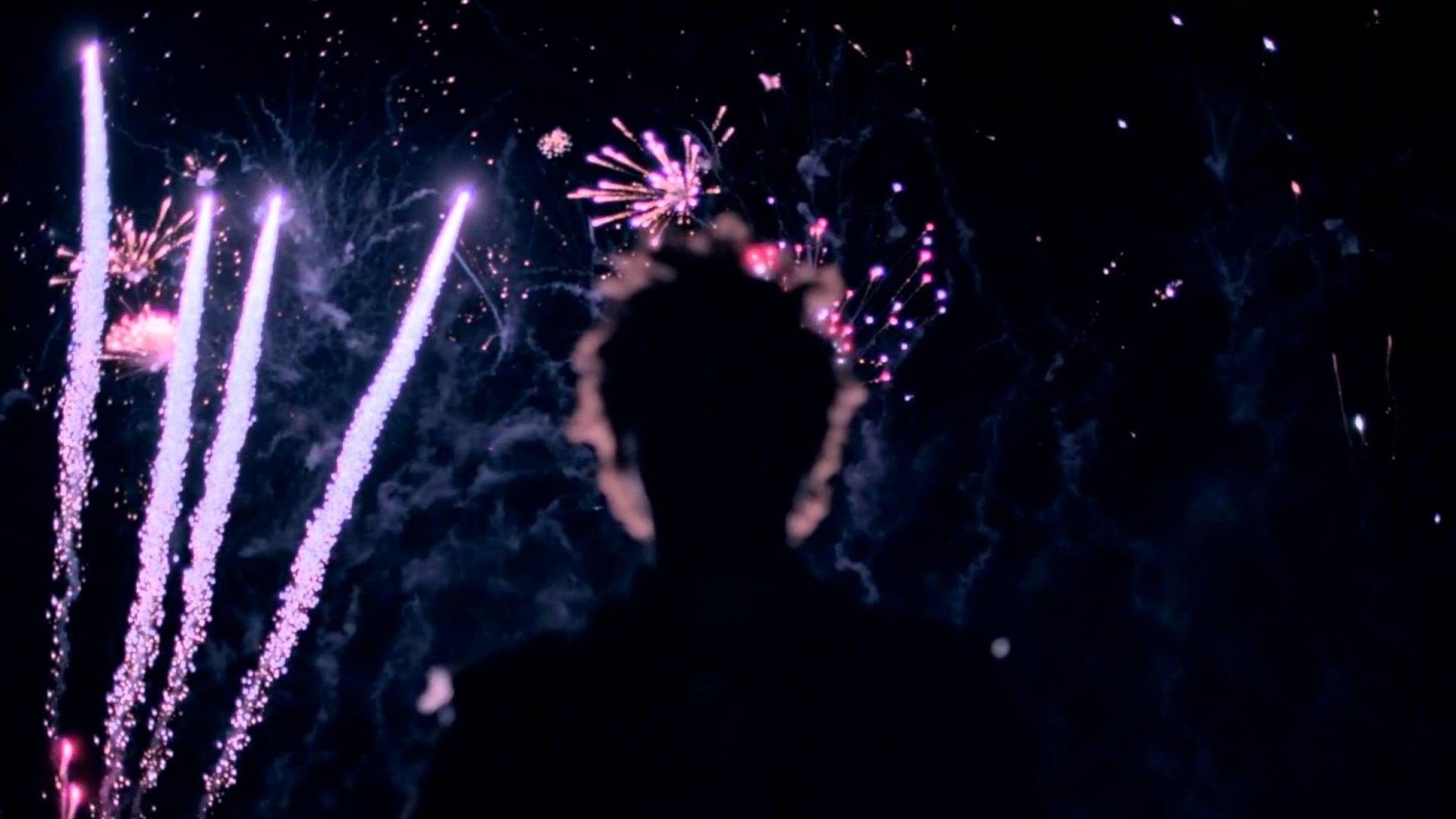 A crowd of people watch fireworks in the night sky - The Weeknd