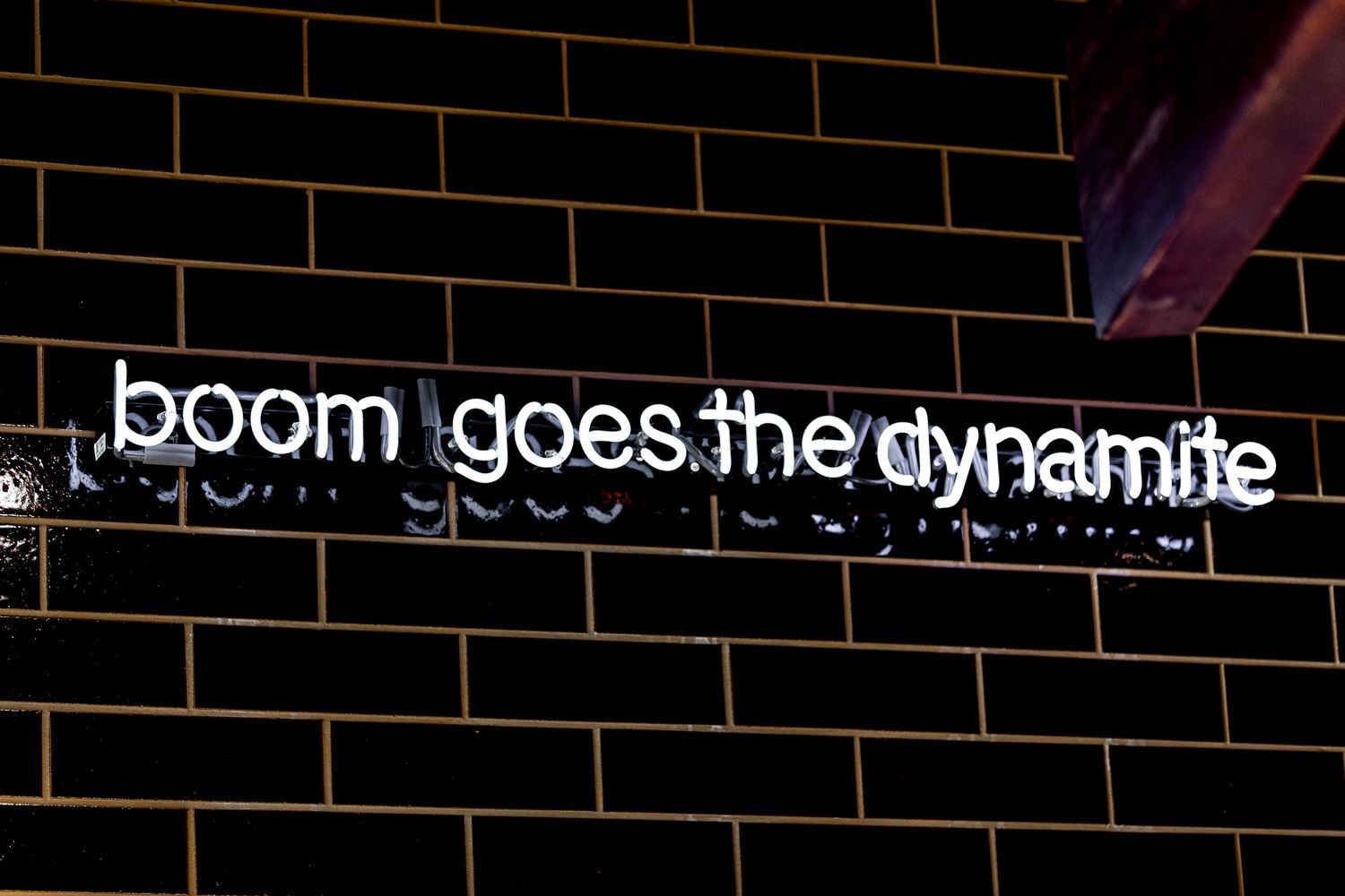 A brick wall with a neon sign that reads 'boom goes the dynamite' - 2000s