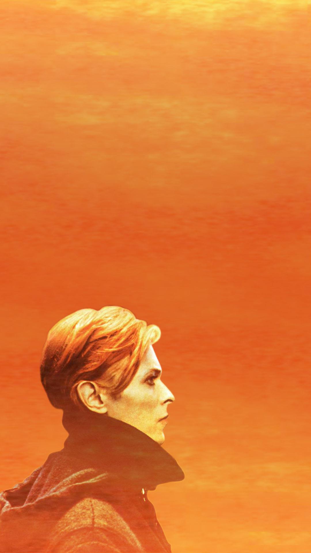 A man with red hair and glasses is standing in front of an orange sky - David Bowie