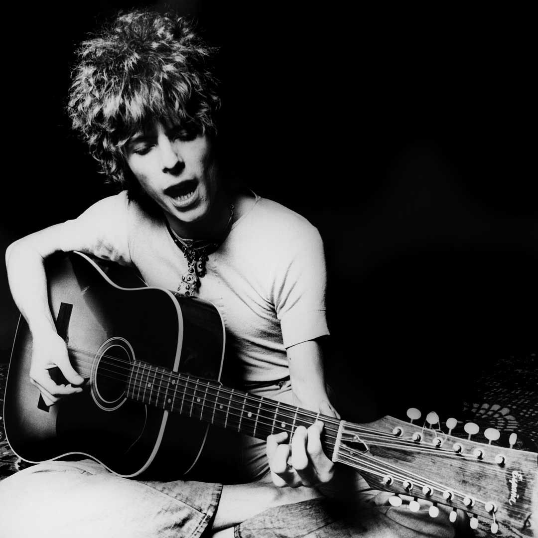 A black and white photograph of the young man playing guitar - David Bowie