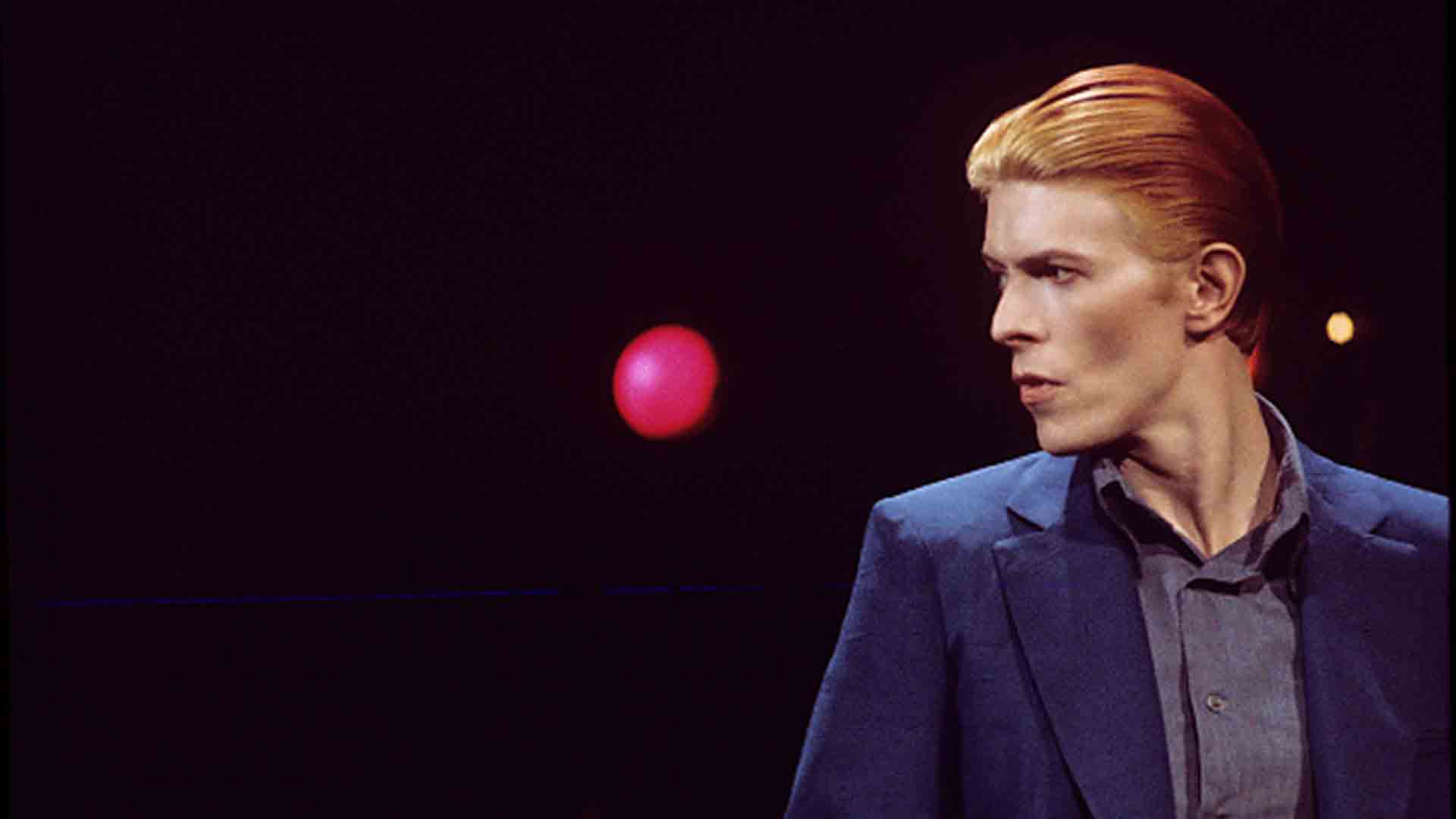 A man with an orange head is standing in the dark - David Bowie